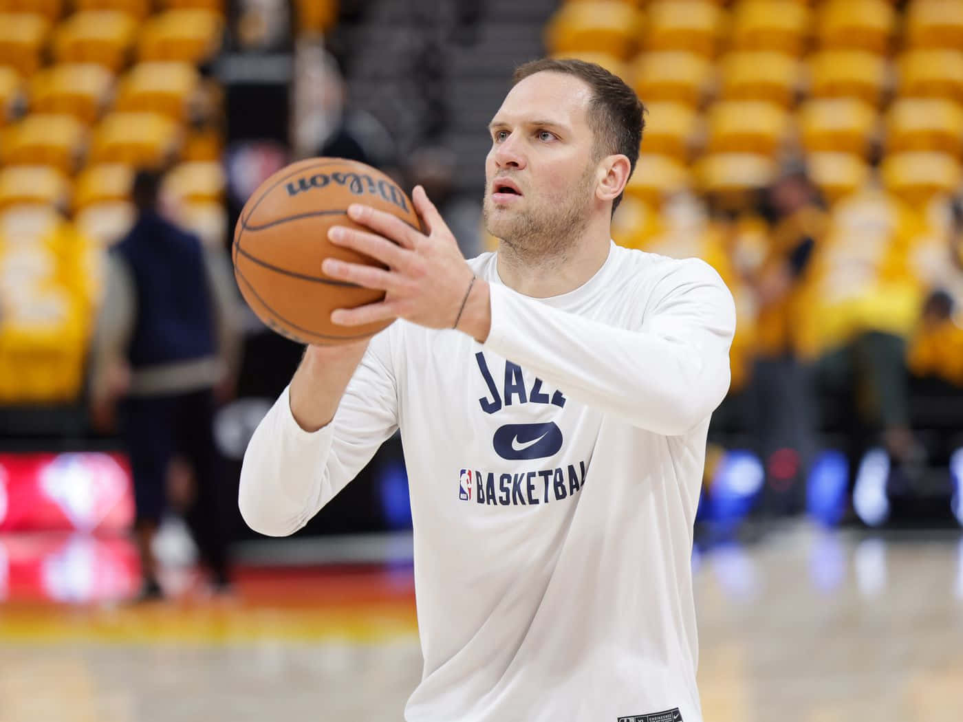 NBA 烏特ah 爵士隊 波揚·博格丹諾維奇 壁紙 — 一名身穿白色爵士練習球衣的籃球運動員，在一個有黃色座位的球場上準備投擲威爾遜籃球。