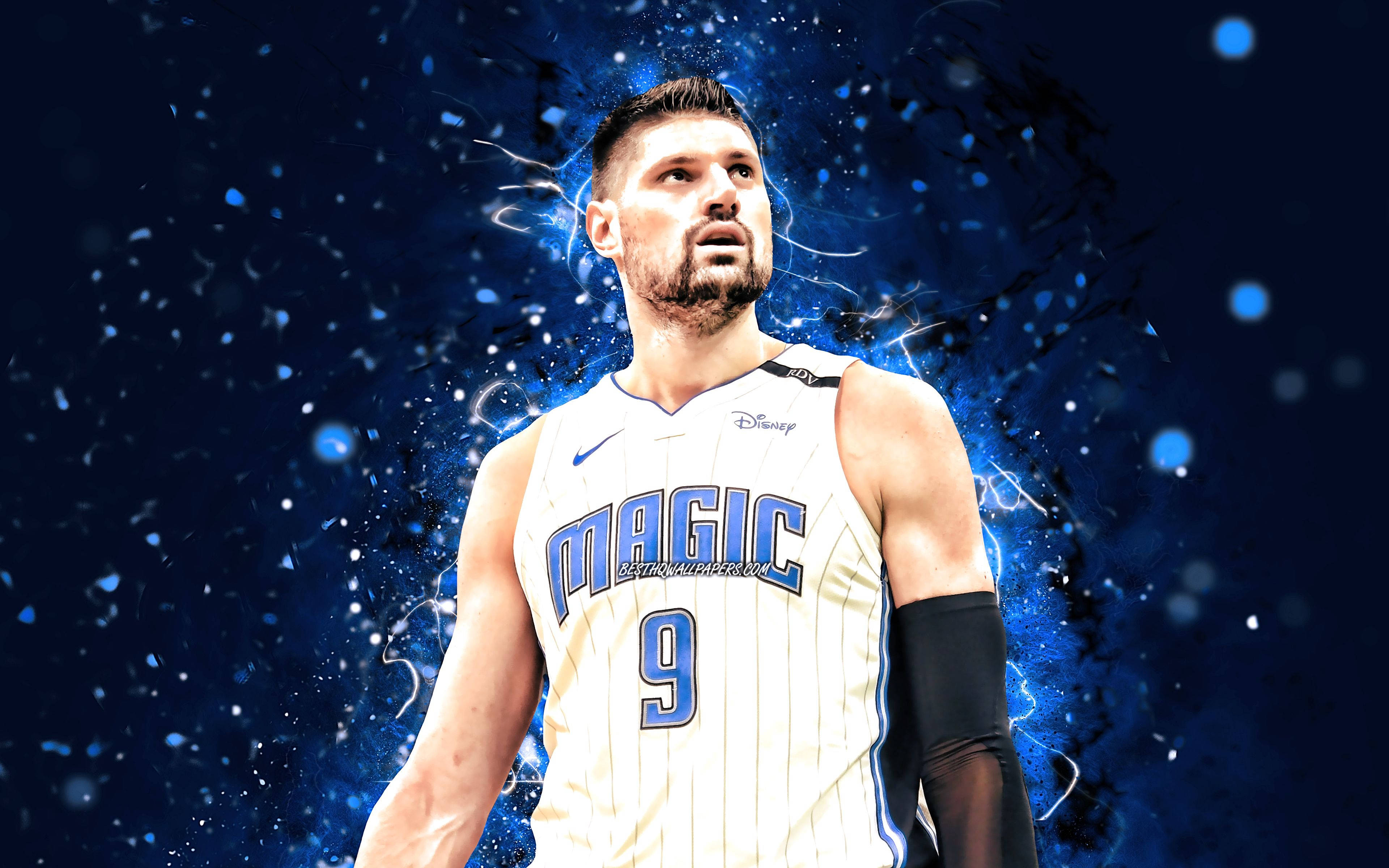 NBA 球員尼古拉·武切維奇奧蘭多魔術隊數位藝術 壁紙 — 一名身穿白色奧蘭多魔術隊球衣的籃球運動員，站在帶有發光粒子的動態藍色電光背景前。
