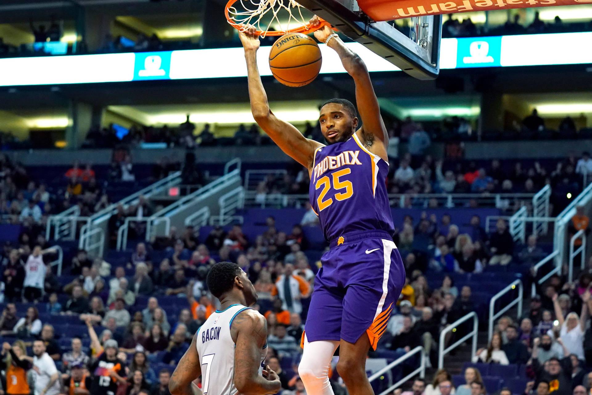 NBA 米卡爾·布里奇斯 拿下灌籃 壁紙 — 一名身穿紫色鳳凰城太陽隊球衣的籃球運動員在擠滿觀眾的場館內大力灌籃，而一名防守球員在下方觀看。