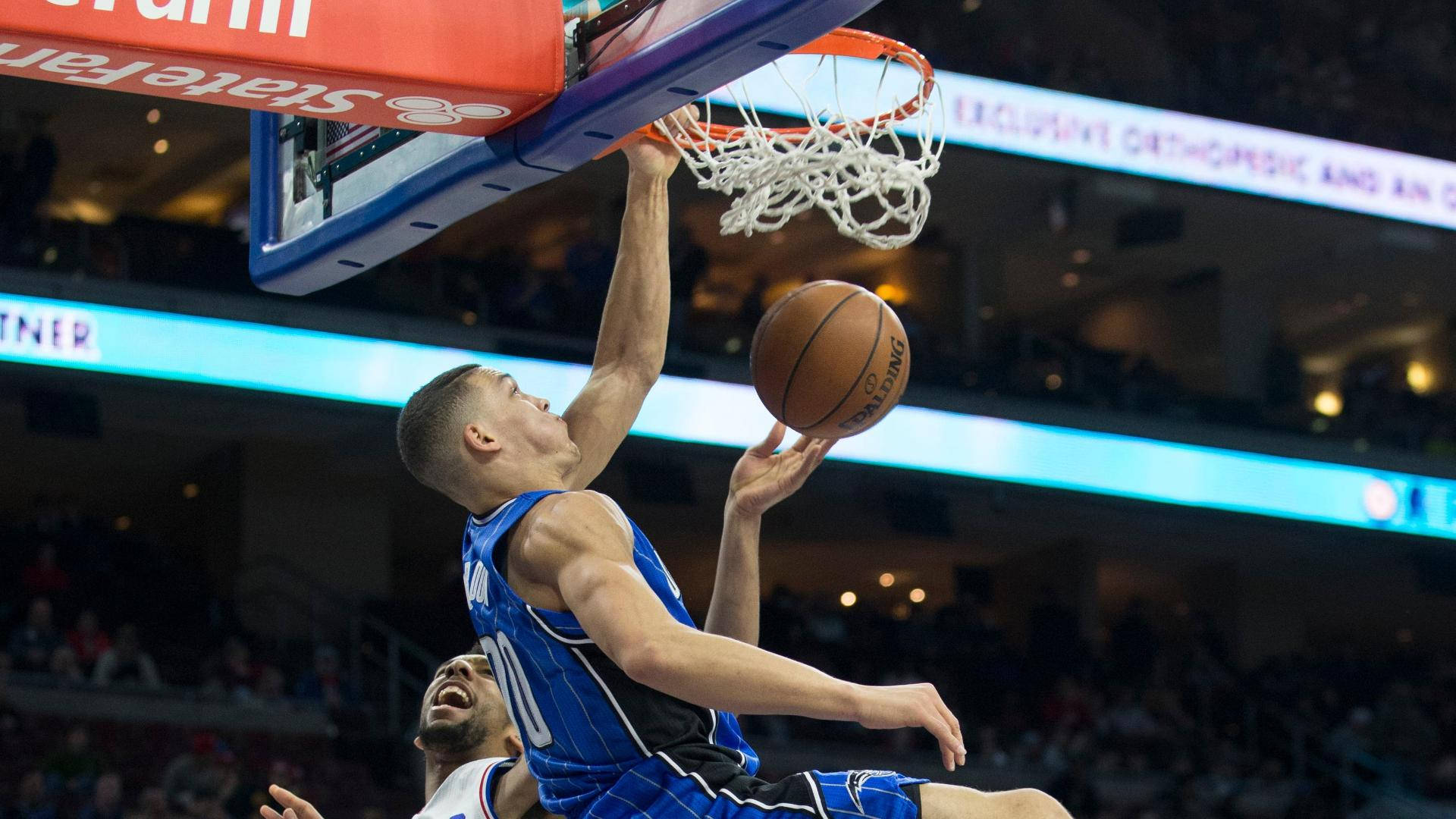NBA 阿隆·戈登 力量前鋒 壁紙 — 一名身穿藍色球衣的籃球運動員在燈光明亮的場館中，在防守球員下方觀看下，專注地灌籃。