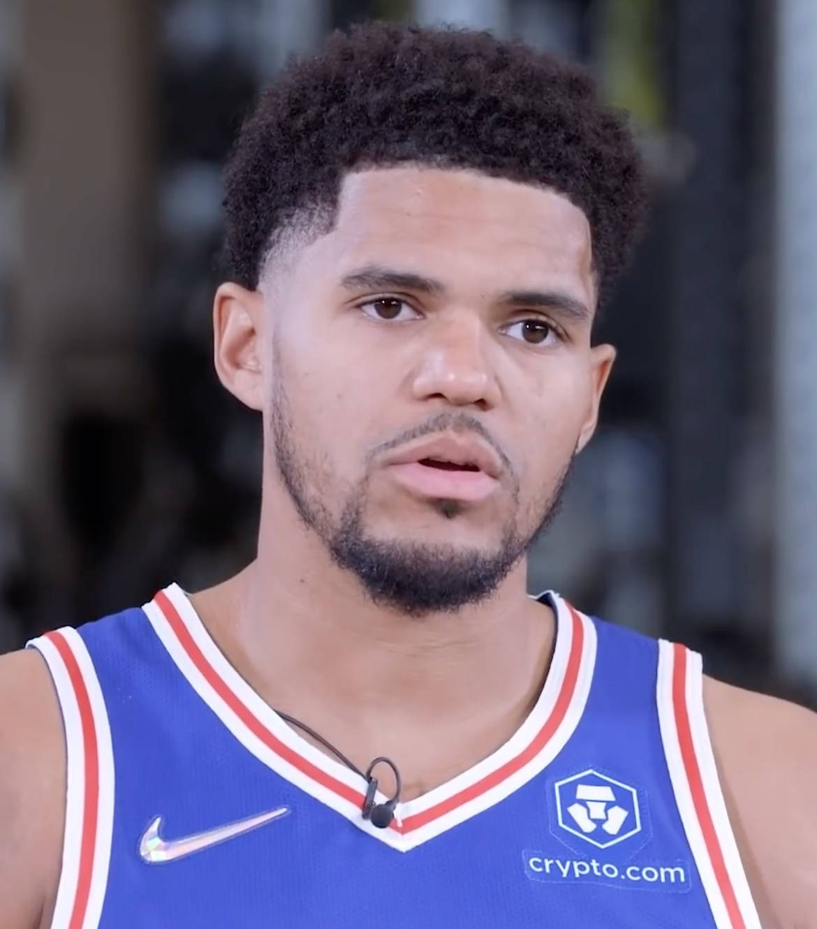NBA球員托拜厄斯·哈里斯費城76人隊面部特寫 壁紙 — 專注的籃球運動員身穿藍、紅、白三色球衣，帶有crypto.com標誌的close-up肖像。