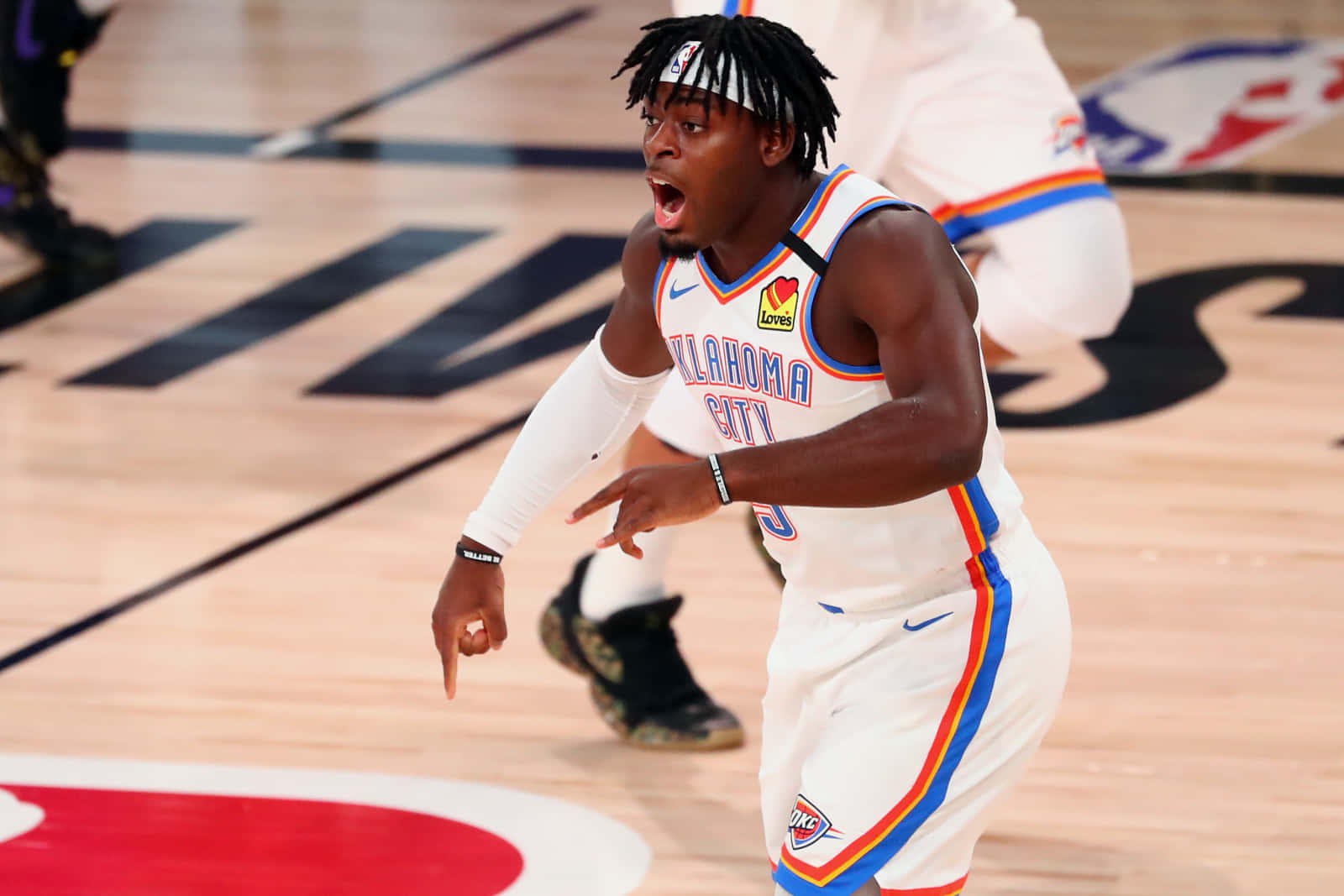 NBA俄克拉荷馬雷霆隊Luguentz Dort怒吼瞬間 壁紙 — 一名身穿奧克拉荷馬城球衣的籃球運動員在拋光木地板的比賽中激烈地大喊。