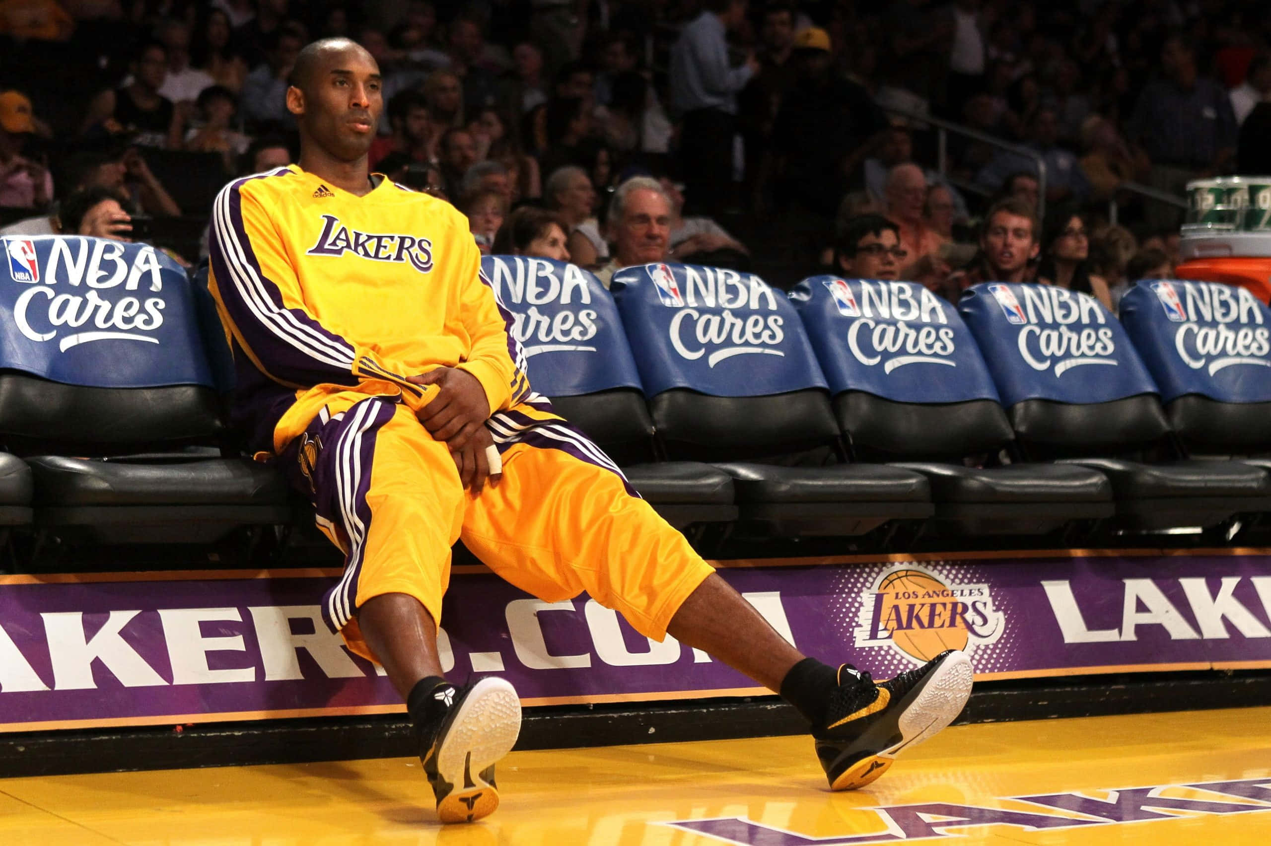 NBA傳奇球星科比·布萊恩特在比賽中 壁紙 — 高比拜仁穿著黃色湖人運動服坐在籃球場的長椅上，在比賽中若有所思。
