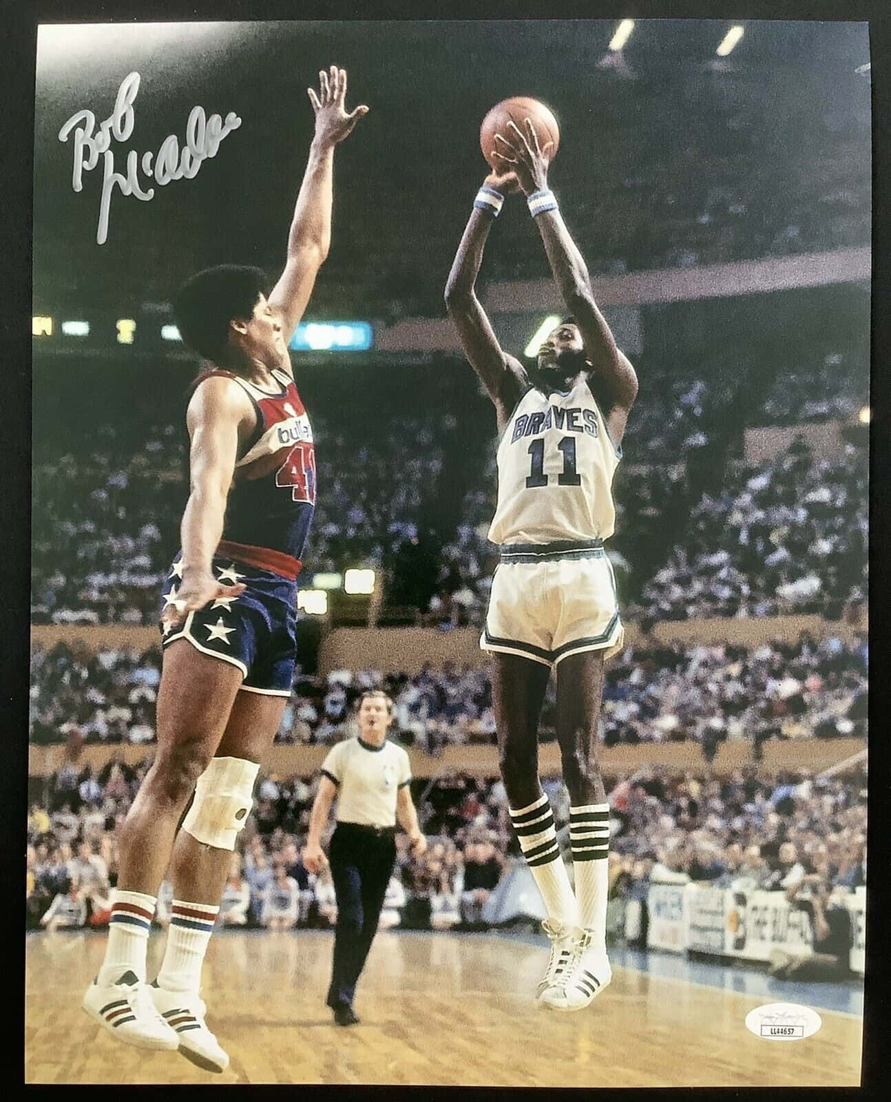NBA傳奇球星鮑勃·麥卡杜與韋斯·恩賽爾激烈對決 壁紙 — Bob McAdoo 身穿白色 Braves 球衣跳起投籃，而身穿藍色星星短褲的防守球員在擠滿觀眾的場館中跳起封阻。