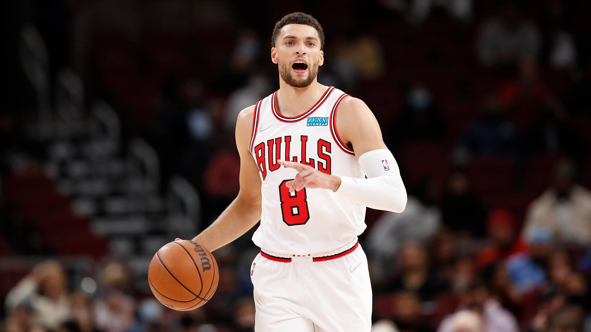 NBA全明星扎克·拉文 壁紙 — 一位芝加哥公牛隊籃球運動員身穿白色球衣，在明亮的場館燈光下，於比賽中專注地運球。
