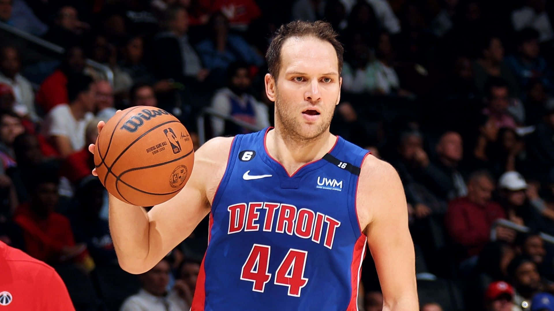 NBA底特律活塞隊博揚·博格達諾維奇 壁紙 — 一位專注的底特律活塞籃球運動員，身穿藍色球衣44號，在比賽中手持籃球，背景是模糊的人群。