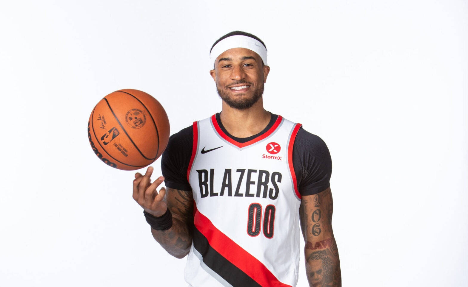 NBA控球後衛加里·佩頓二世 壁紙 — 一位微笑的籃球運動員穿著 Blazers 球衣，在純白背景下旋轉籃球。