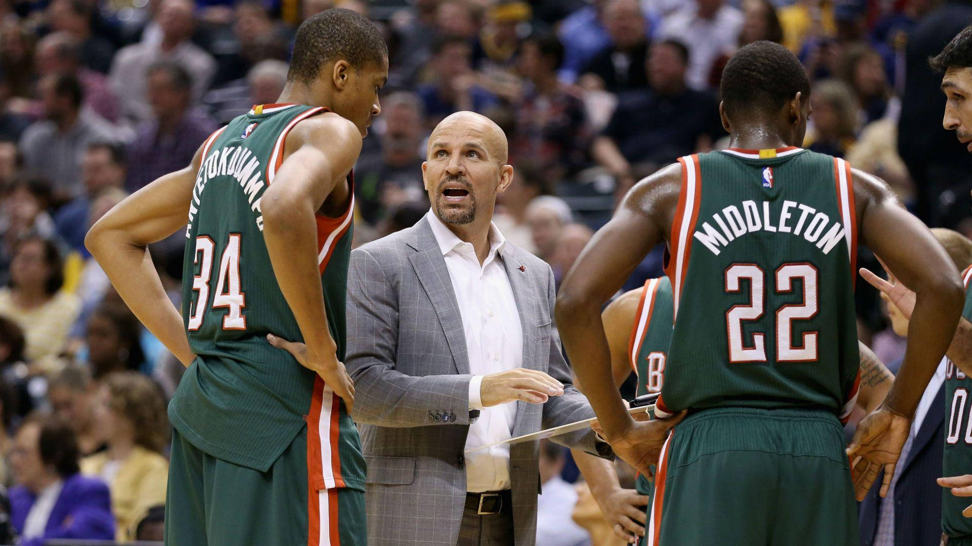 NBA教練賈森·基德指導年輕的揚尼斯·阿德托昆博 壁紙 — 一位身穿灰色西裝的籃球教練在比賽中熱情地與兩名身穿綠色球衣的球員交談，背景是模糊的人群。