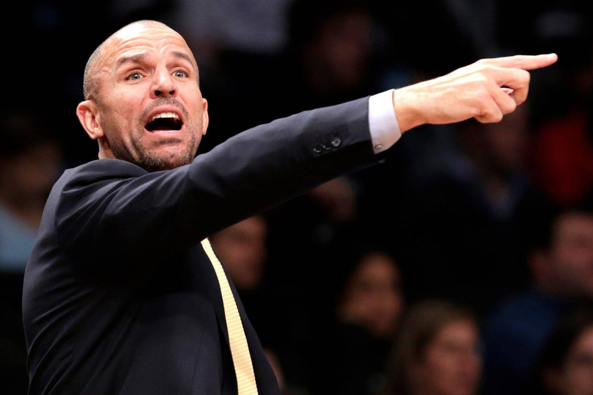 NBA教練賈森·基德指揮 壁紙 — 一位光頭籃球教練穿著深色西裝，在比賽中緊急大喊並指著，身後有模糊的觀眾。