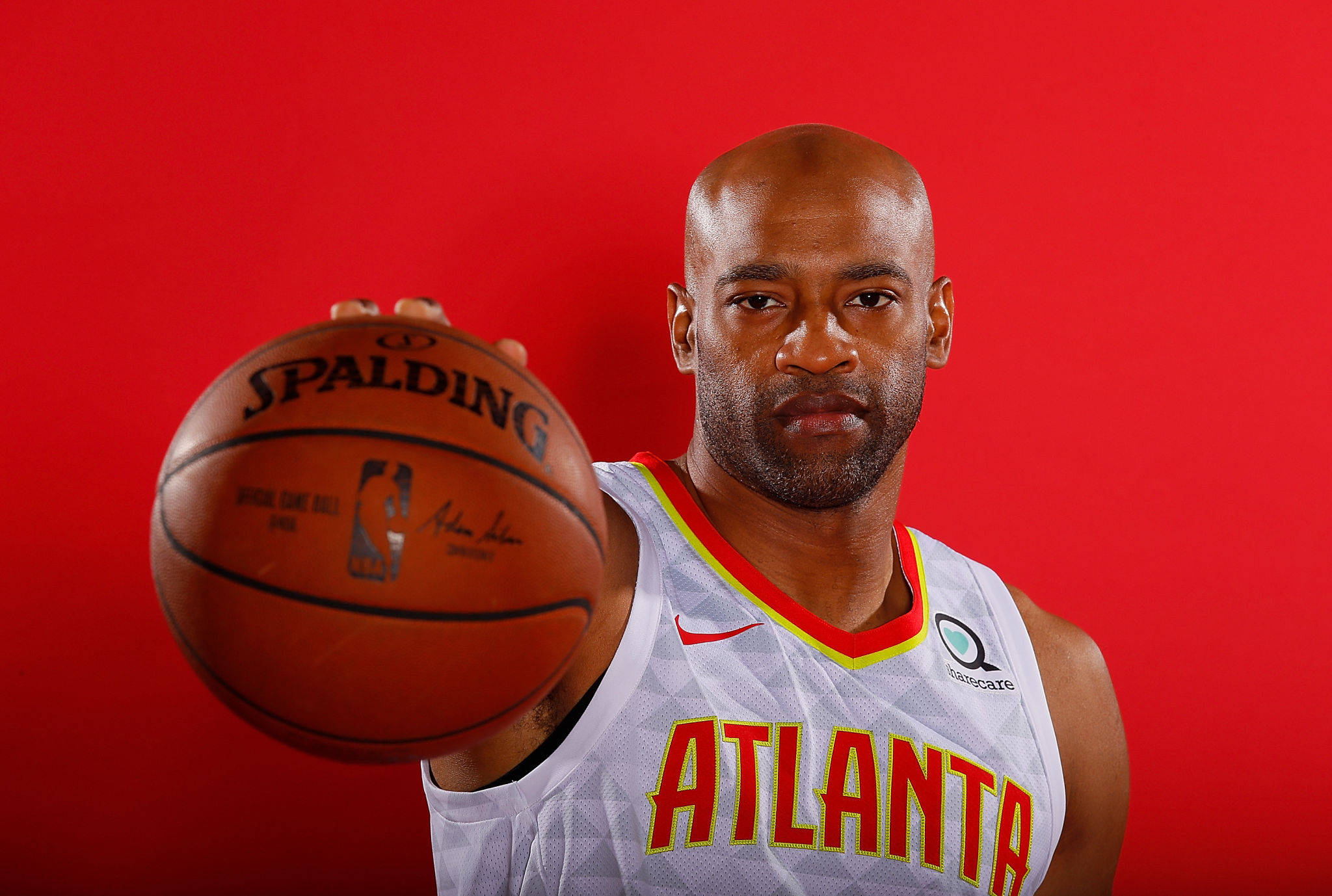 NBA文斯·卡特肖像 壁紙 — 一位光頭籃球運動員穿著亞特蘭大球衣，在純紅色背景前拿著一個Spalding籃球。