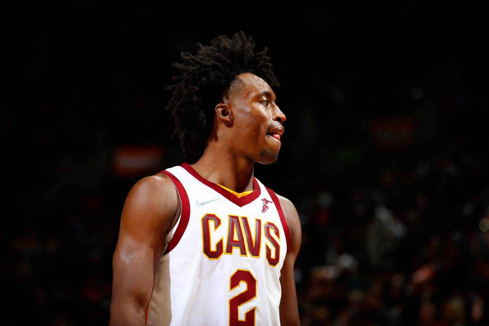 NBA明星2號科林·塞克森 壁紙 — 一位專注的籃球運動員身穿白色Cavs球衣，背號2號，站在燈光昏暗的球場上，目光向上凝視。
