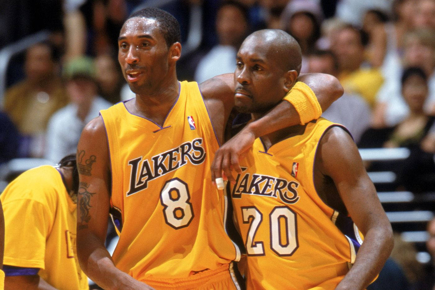NBA洛杉磯湖人隊加里·佩頓父 壁紙 — 兩名身穿黃色球衣的湖人籃球運動員在比賽中擁抱，背景有觀眾。