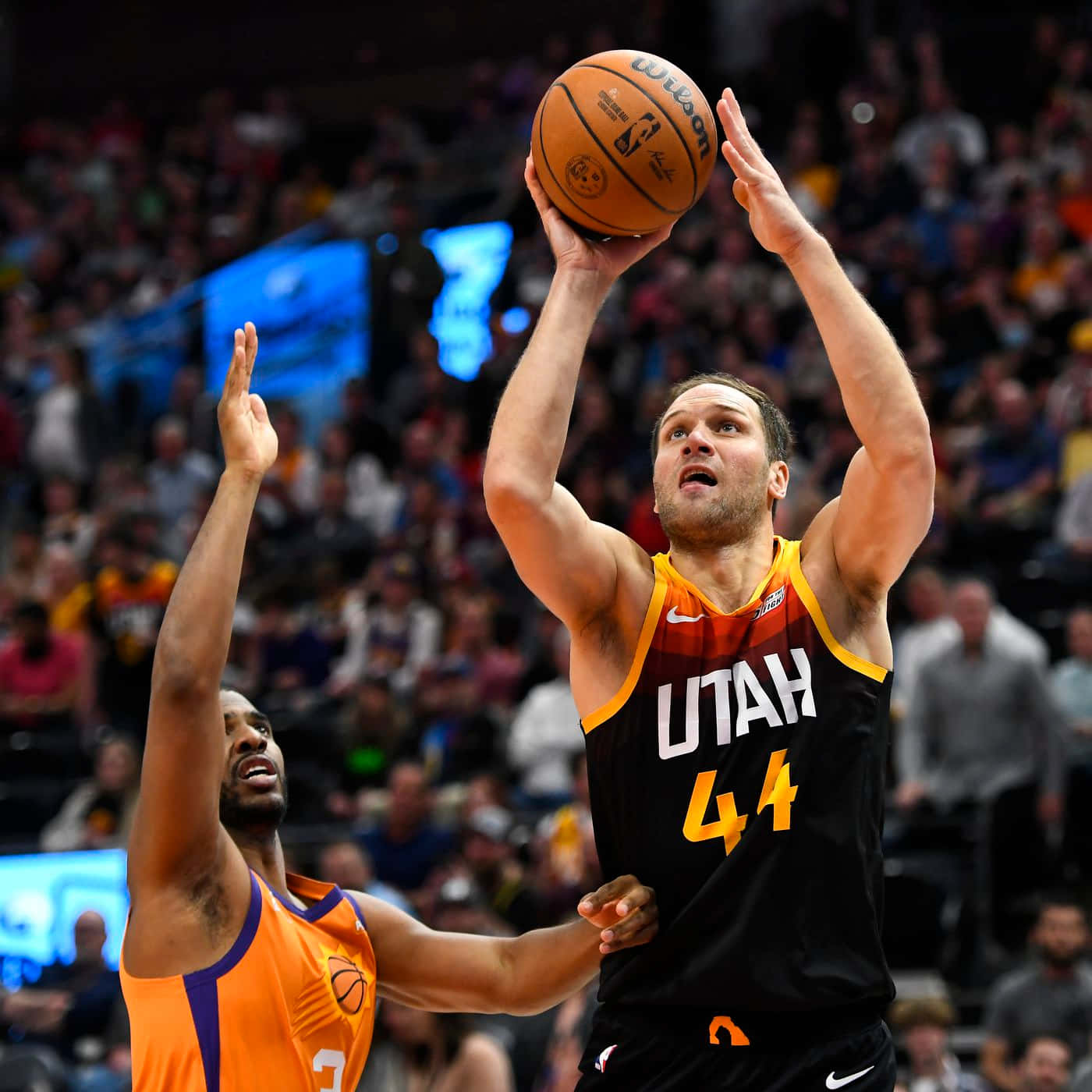 NBA猶他爵士隊44號博揚·博格達諾維奇 壁紙 — 一位身穿黑黃球衣的猶他爵士球員正在投籃，而一位身穿橙色球衣的鳳凰城太陽防守球員在場館燈光下干擾投籃。