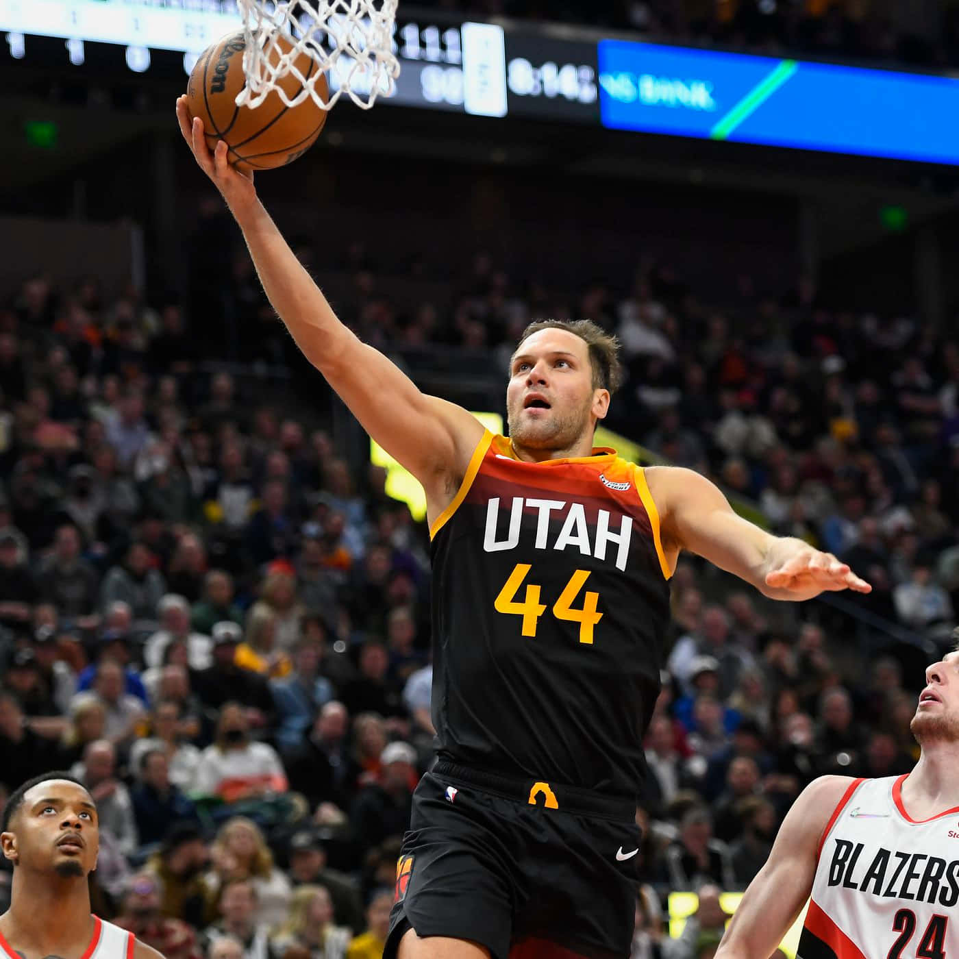 NBA猶他爵士隊博揚·博格達諾維奇上籃 壁紙 — 一位猶他爵士隊球員身穿黑橙色球衣，在座無虛席的球場比賽中專注地灌籃。