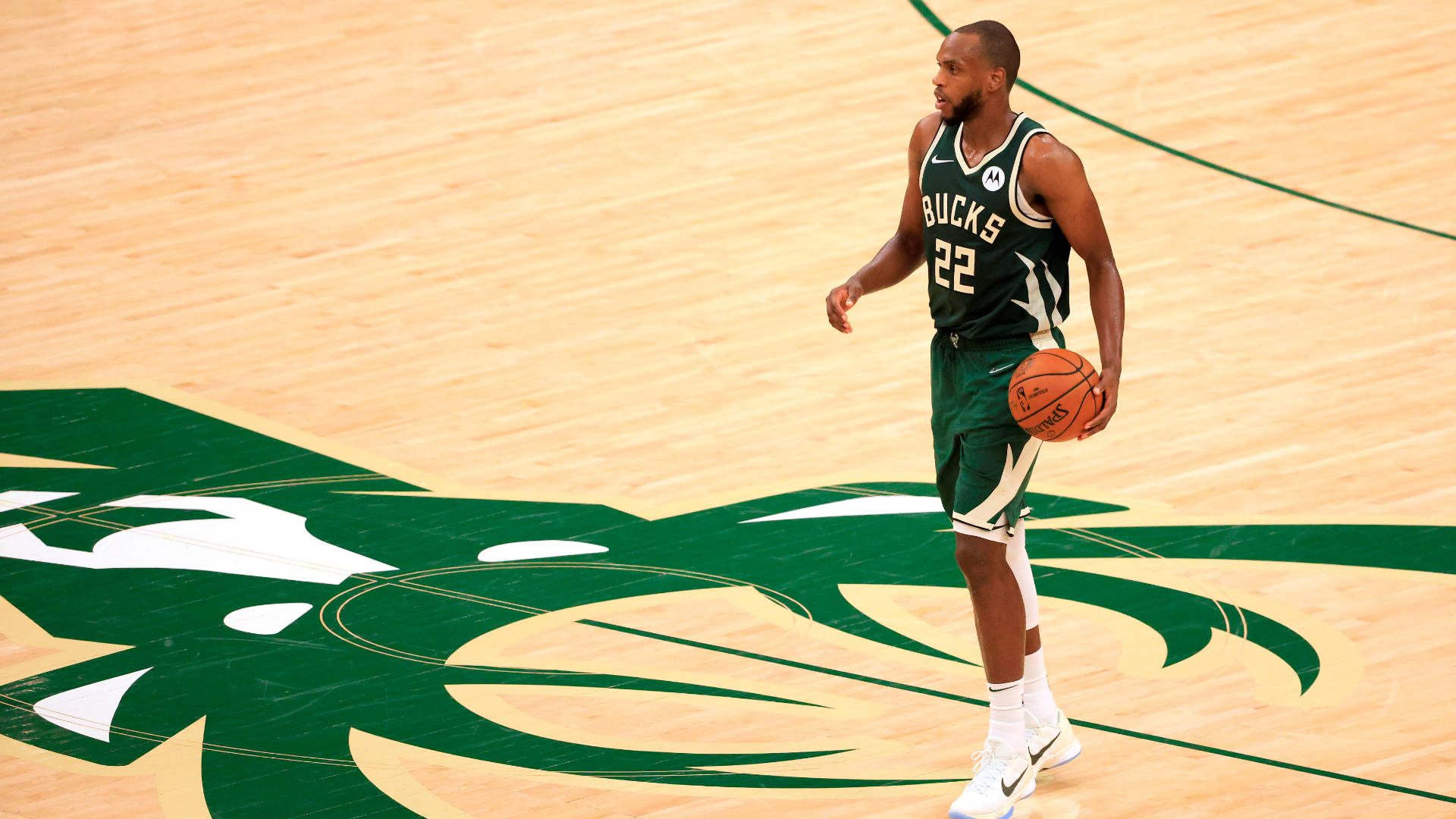 NBA球員克里·米德尔頓 壁紙 — 一位身穿綠色球衣的密爾沃基公鹿籃球運動員在硬木球場上拿著球，球場上有球隊標誌。