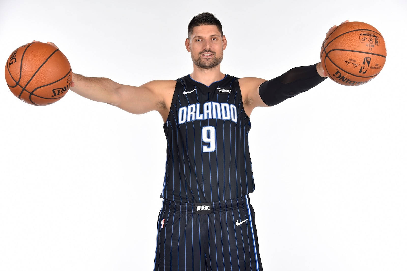 NBA球員尼古拉·武切维奇奧蘭多魔術隊寫真 壁紙 — 一名身穿奧蘭多魔術隊球衣的籃球運動員，在純白色背景前伸出雙手各持一個籃球。