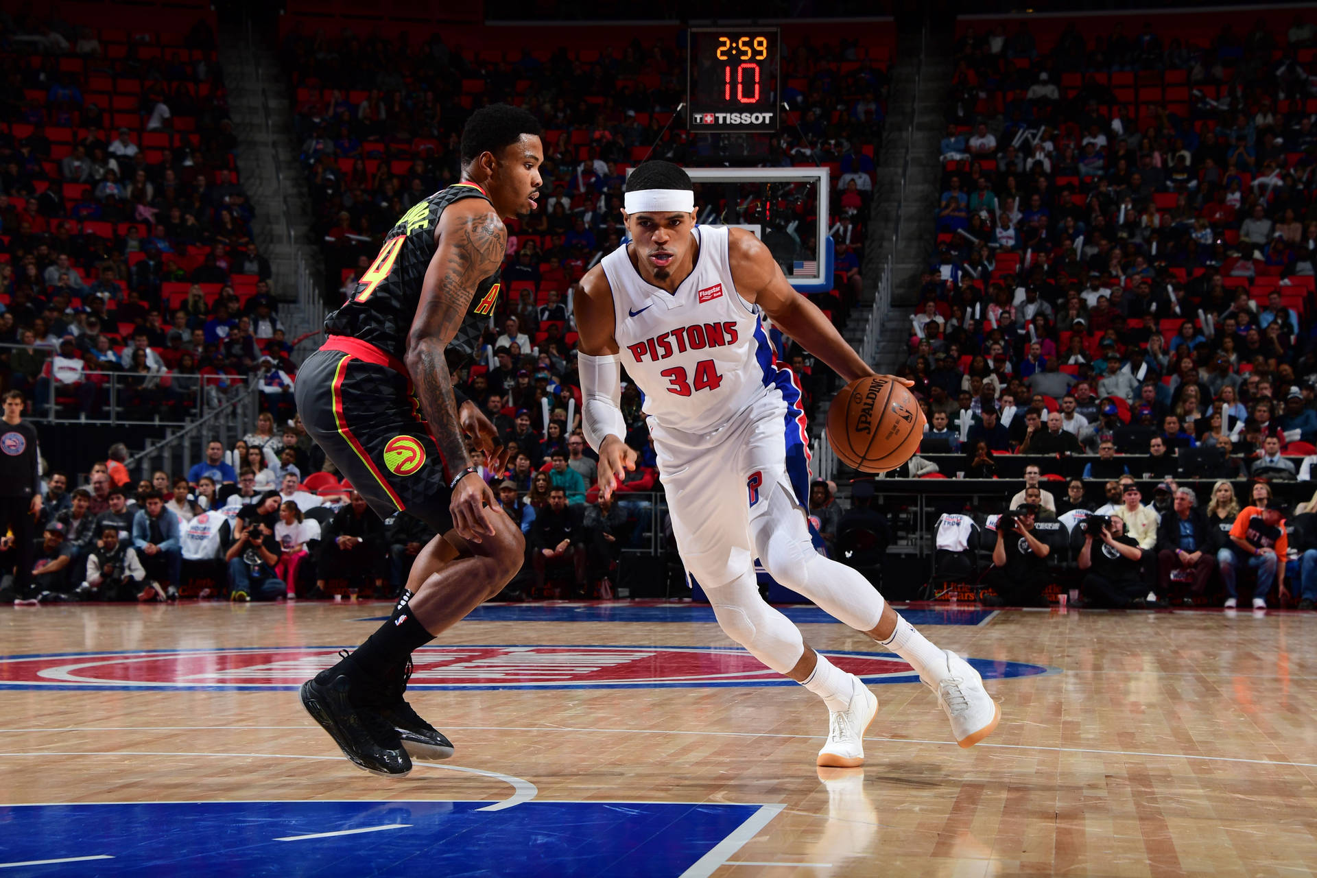 NBA球員底特律活塞隊托拜厄斯·哈里斯 壁紙 — 一位身穿白色球衣的底特律活塞隊球員在擠滿觀眾的籃球場上運球，同時受到對方球員的防守。