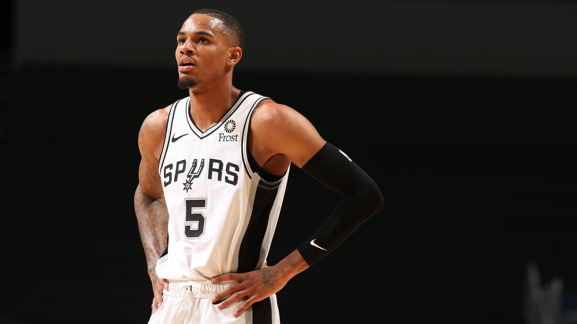 NBA球員德章泰·穆雷 壁紙 — 一位專注的籃球運動員身穿Spurs球衣，雙手叉腰站在深色背景前。