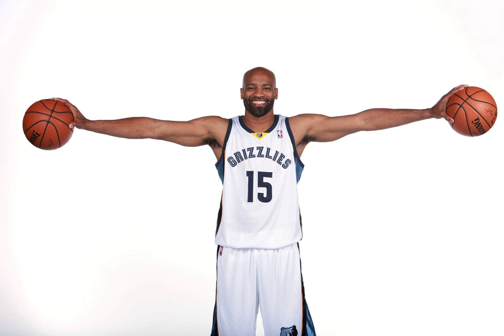 NBA球員文斯·卡特 壁紙 — 一名微笑的籃球運動員身穿灰熊隊球衣，雙臂張開，每隻手各持一個球，背景為純白色。