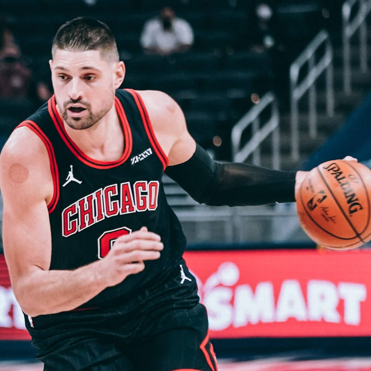 NBA球員芝加哥公牛隊尼古拉·武切維奇運球 壁紙 — 一名專注的籃球運動員身穿黑色芝加哥球衣，在明亮的場館燈光下於比賽中激烈運球。
