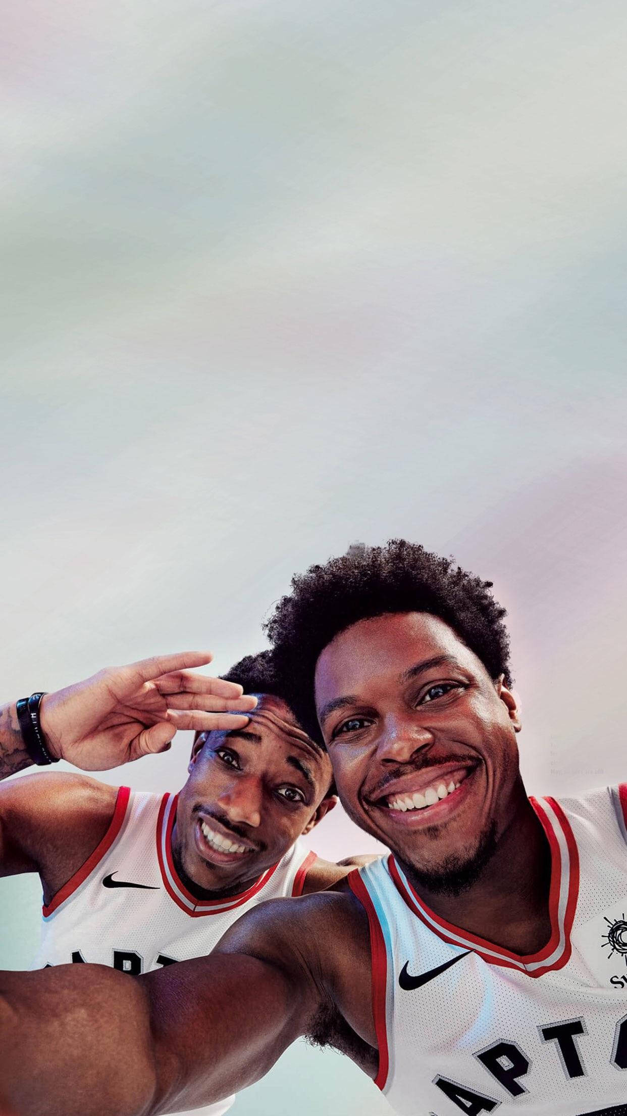 NBA球星凱爾·洛瑞與德馬爾·德羅贊自拍時光 壁紙 — 兩名身穿白色Raptors球衣的籃球運動員微笑著在柔和嘅粉彩天空下自拍。