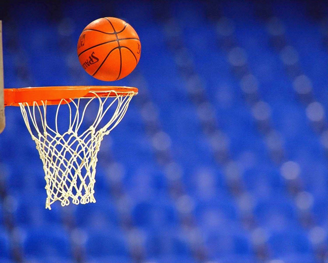 NBA球隊爭奪冠軍 壁紙 — 一個充滿活力的橙色籃球完美地掛在白色網中，背景是模糊的藍色體育場。