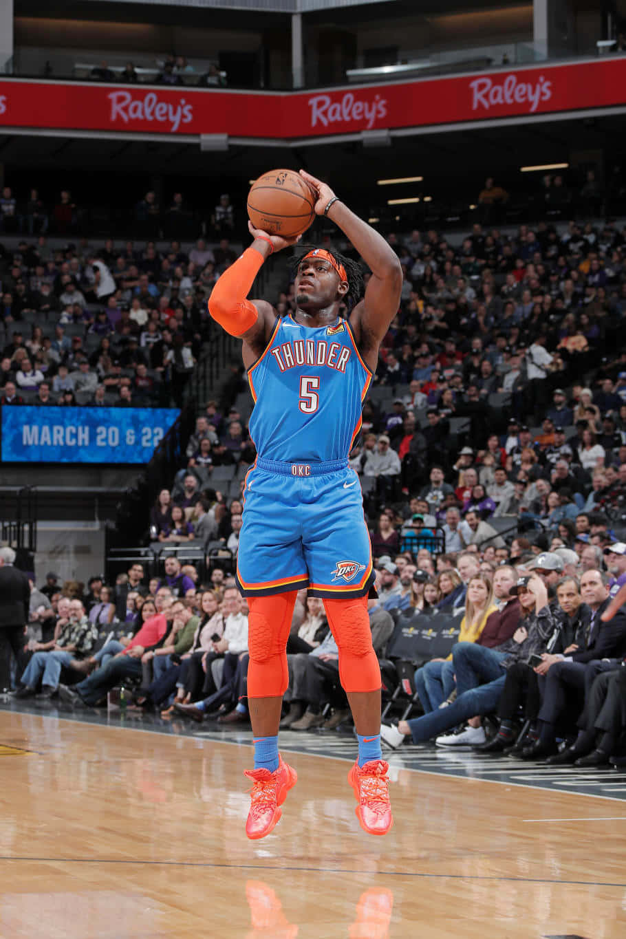 NBA盧根茲·多特三分球 壁紙 — 一名身穿藍色和橙色雷霆隊球衣的籃球運動員在擠滿觀眾的場館中跳起投籃。