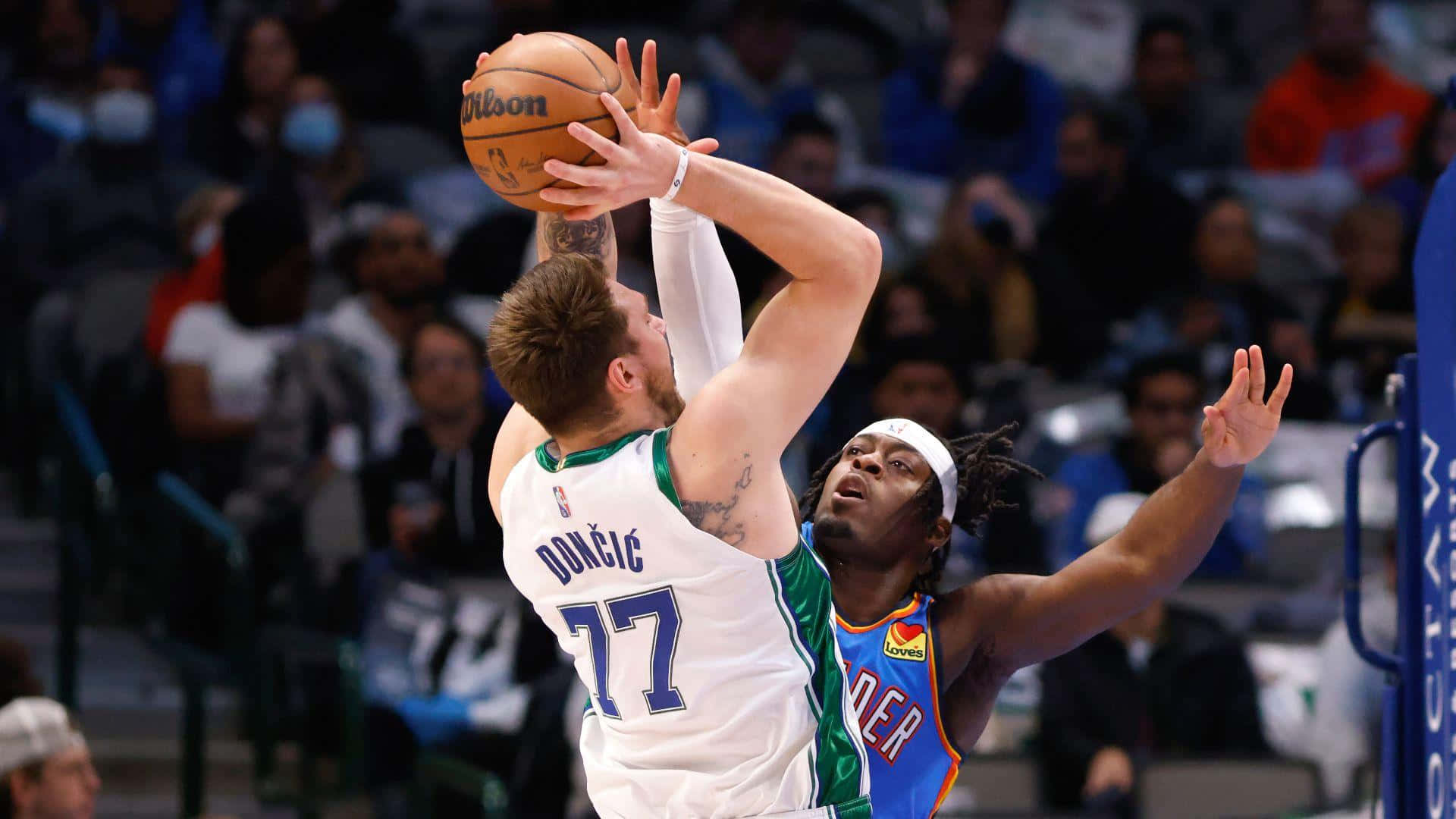 NBA盧根茲·多特封蓋盧卡·東契奇 壁紙 — 一名身穿白色球衣、號碼77的籃球運動員正在投籃，同時被一名身穿藍橙色球衣的對手防守。