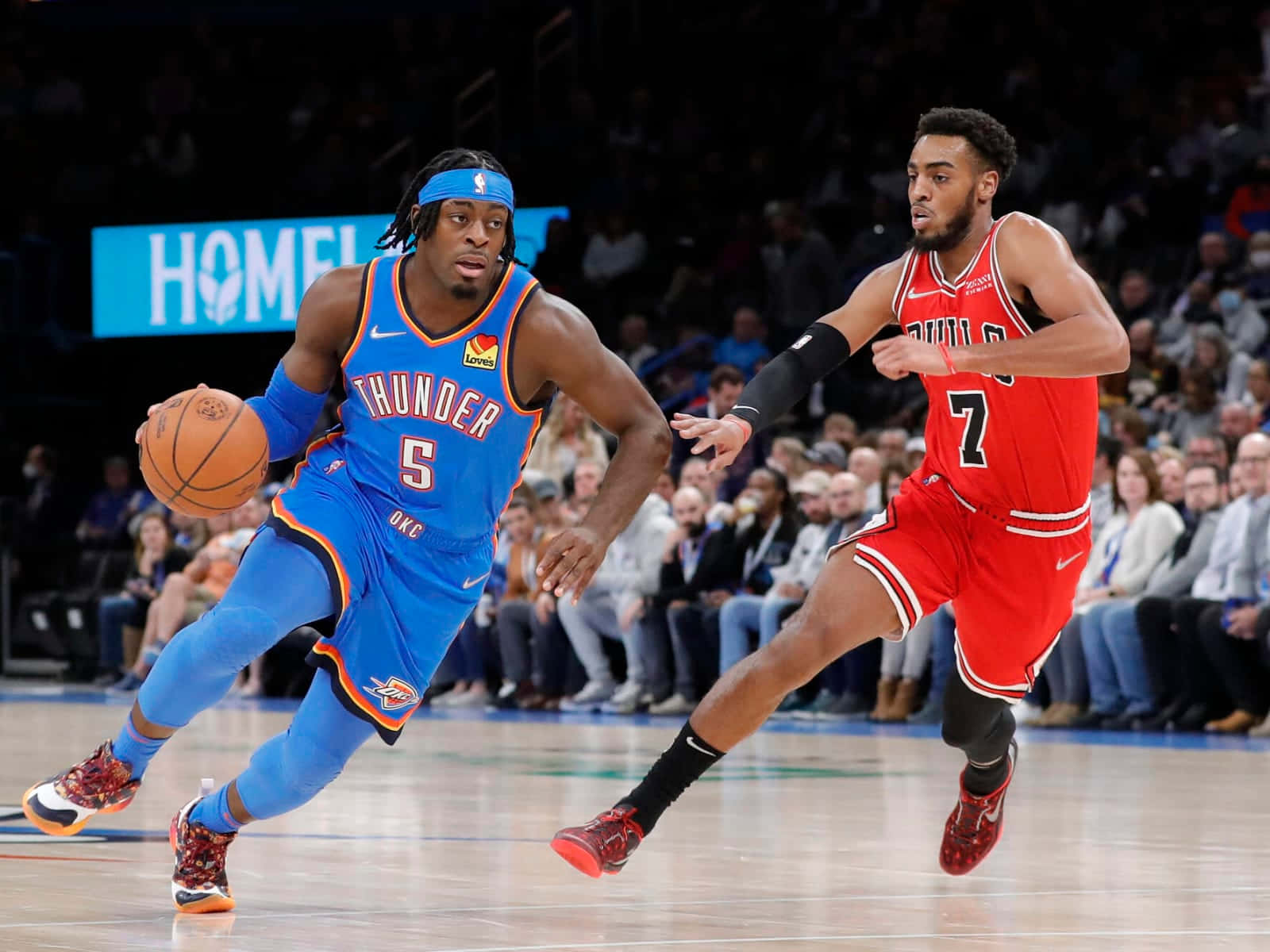 NBA盧根茲·多特與特洛伊·布朗Jr. 壁紙 — 一名身穿藍色雷霆隊球衣的籃球運動員在燈光明亮的球場上運球，同時被一名紅色公牛隊球員緊密防守。