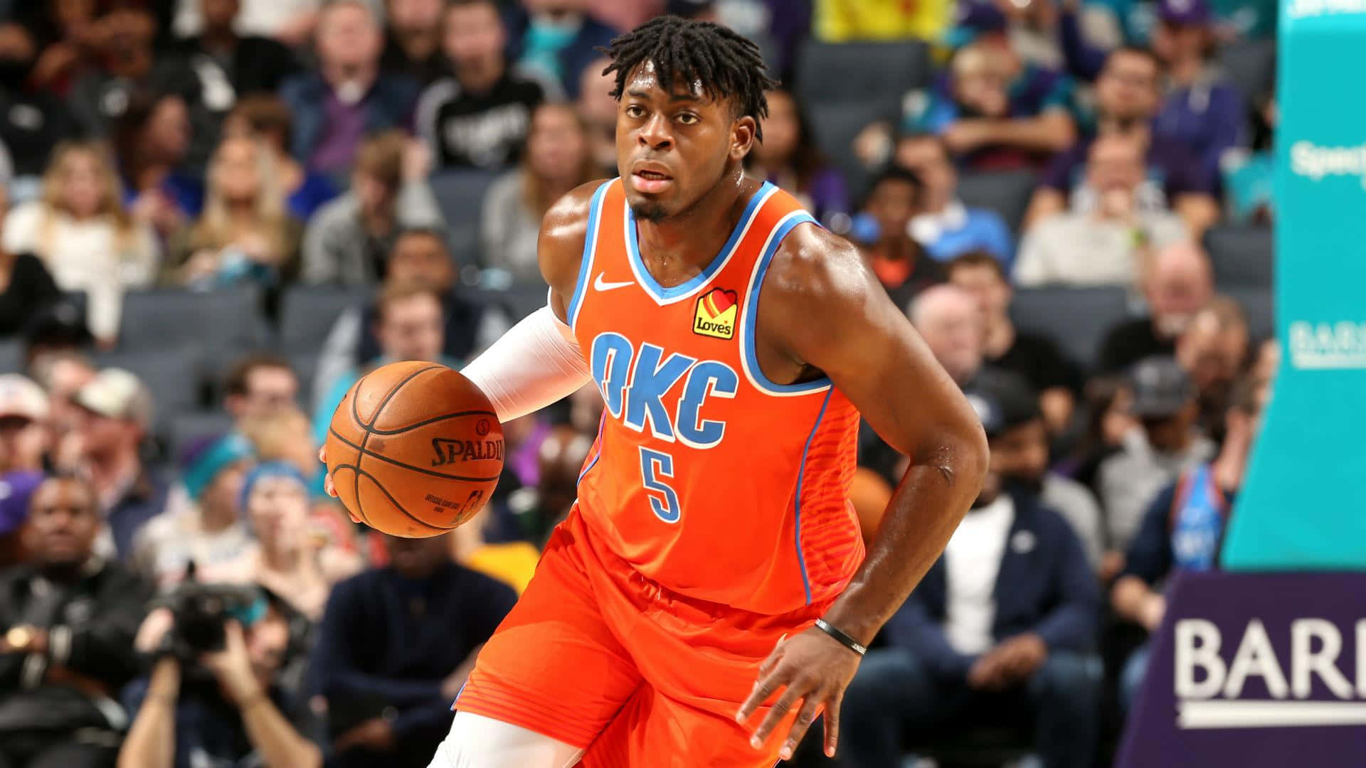 NBA盧根茲·多特身穿橙色奧克拉荷馬城雷霆隊球衣 壁紙 — 一名身穿橙色OKC球衣的籃球運動員在比賽中激烈運球，背景是模糊的人群。