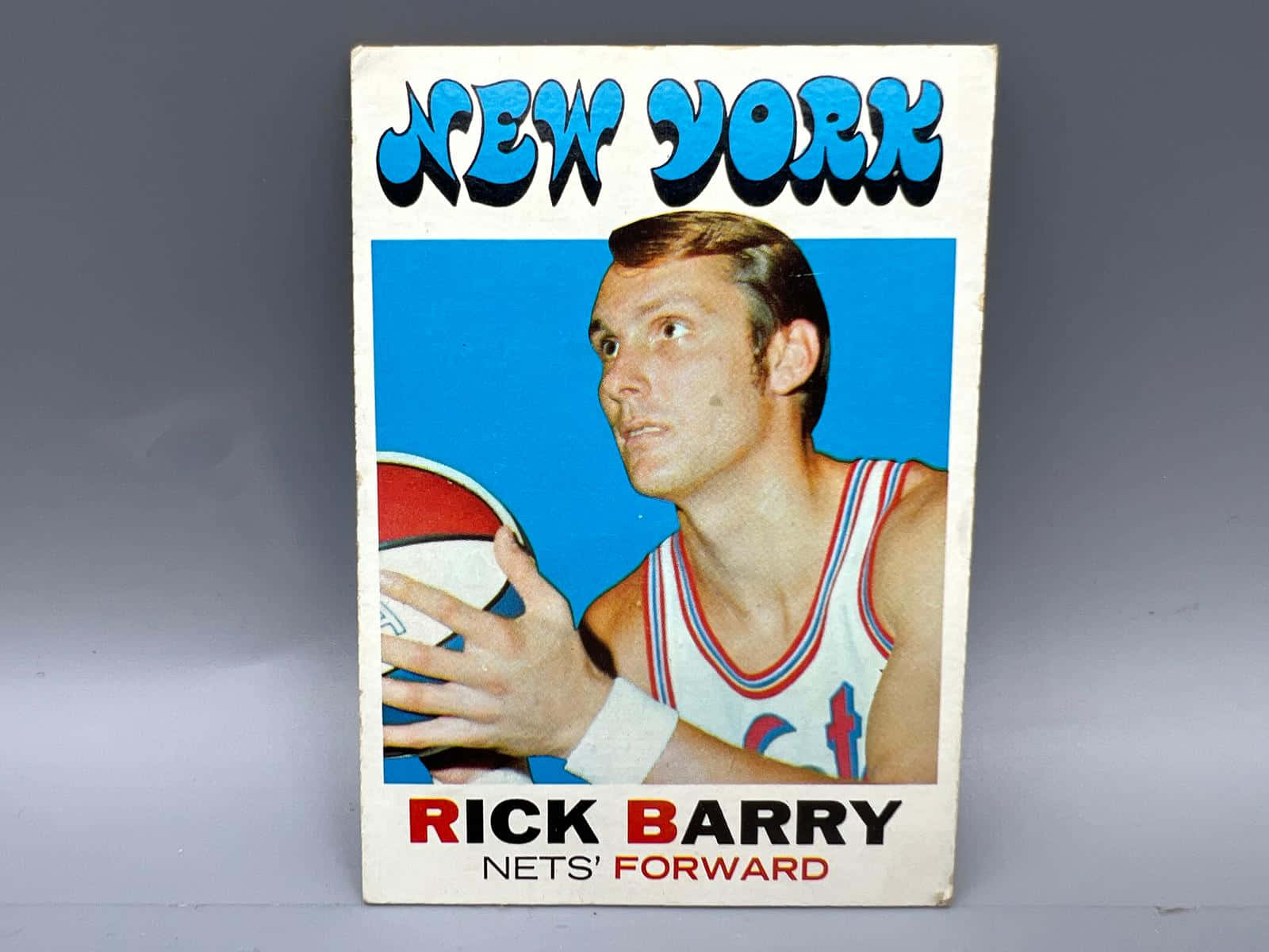 NBA紐約網隊瑞克·巴里海報 壁紙 — 1970年代復古籃球卡，Rick Barry身穿紐約網隊球衣，在藍色背景前持球。