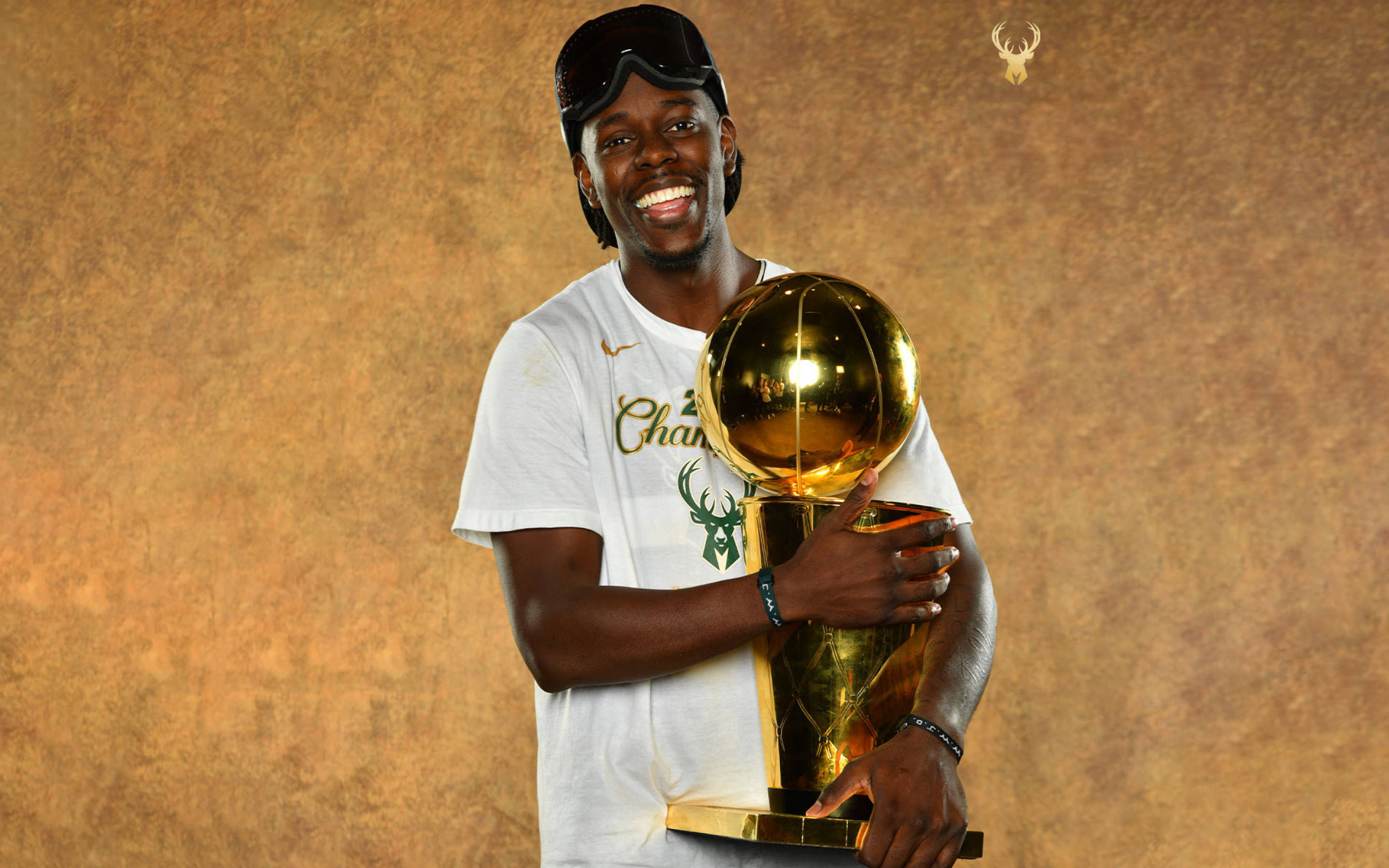 NBA總決賽得主朱·霍利迪 壁紙 — 一位喜悅的籃球運動員在溫暖的紋理背景前，自豪地捧著閃閃發光的金色NBA冠軍獎盃，笑容燦爛。