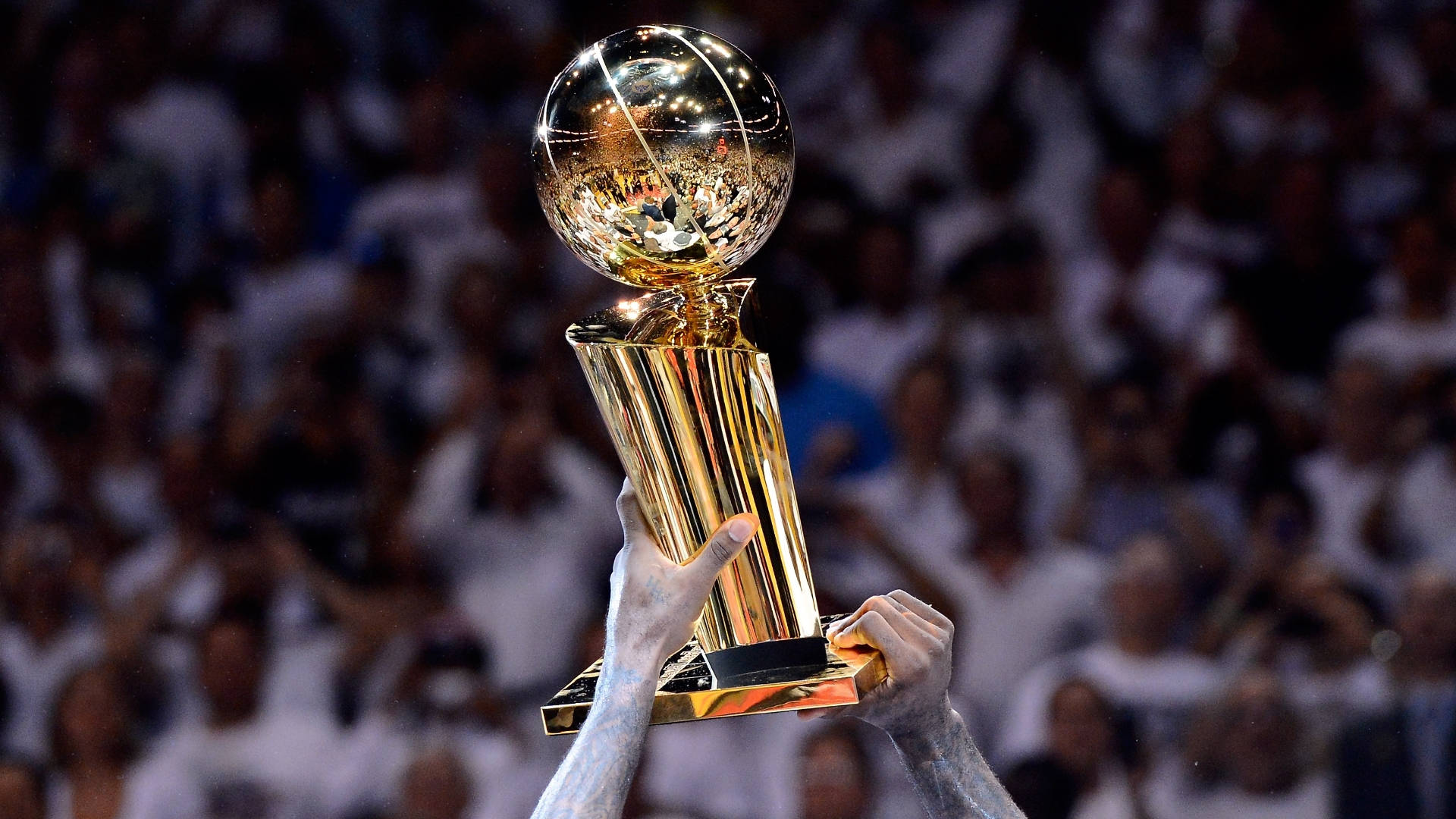 NBA總決賽金獎盃獎項 壁紙 — 一個閃閃發光的金色籃球獎盃在擠滿人的場館中，勝利地高舉在歡呼的人群之上。
