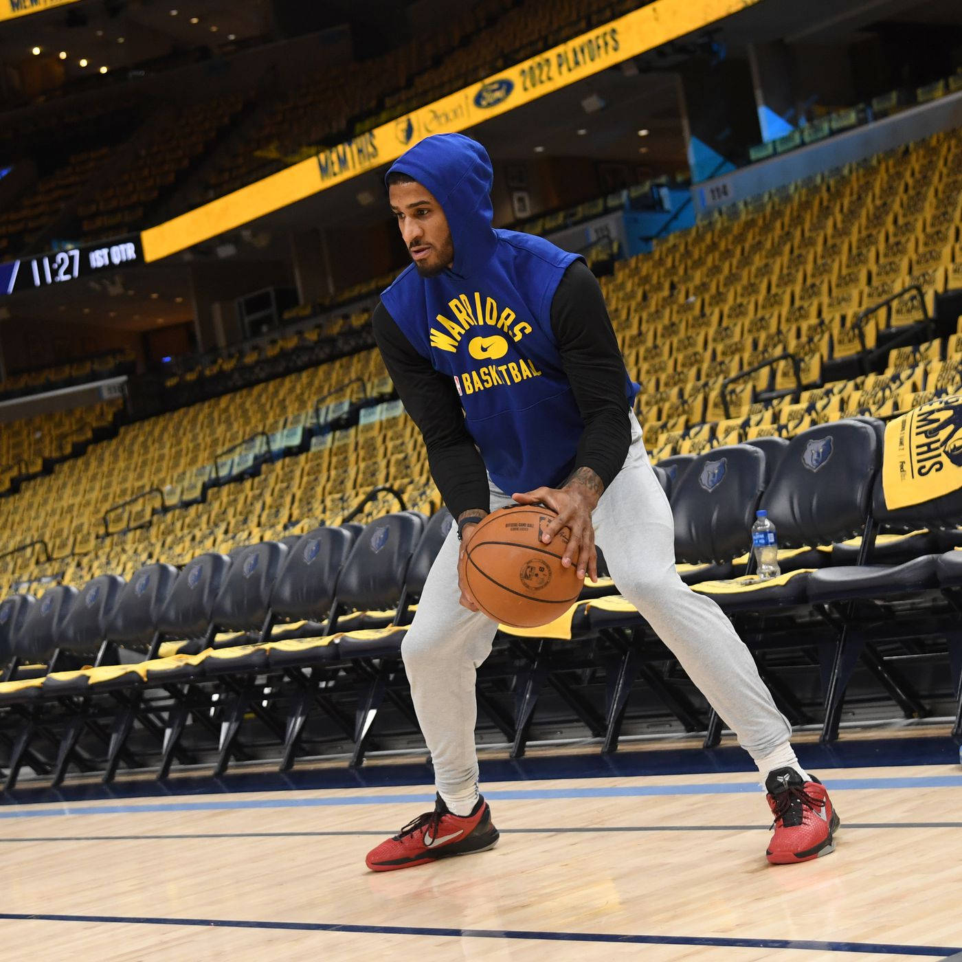 NBA訓練中的加里·佩頓 壁紙 — 一名身穿藍色連帽衫和灰色運動褲的籃球運動員在一個空曠的球場上運球，球場有黃色座位和頭頂上的「2022 PLAYOFFS」標牌。