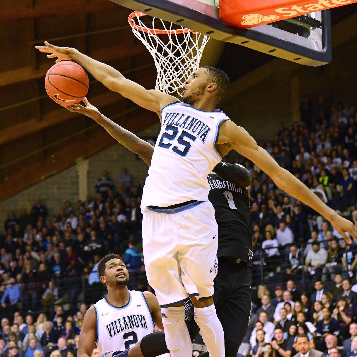 NCAA 維拉諾瓦野貓隊 米卡爾·布里奇斯 壁紙 — 一位身穿白色25號球衣的維拉諾瓦大學籃球運動員跳向籃框準備灌籃，而喬治城大學的防守球員試圖阻擋他。
