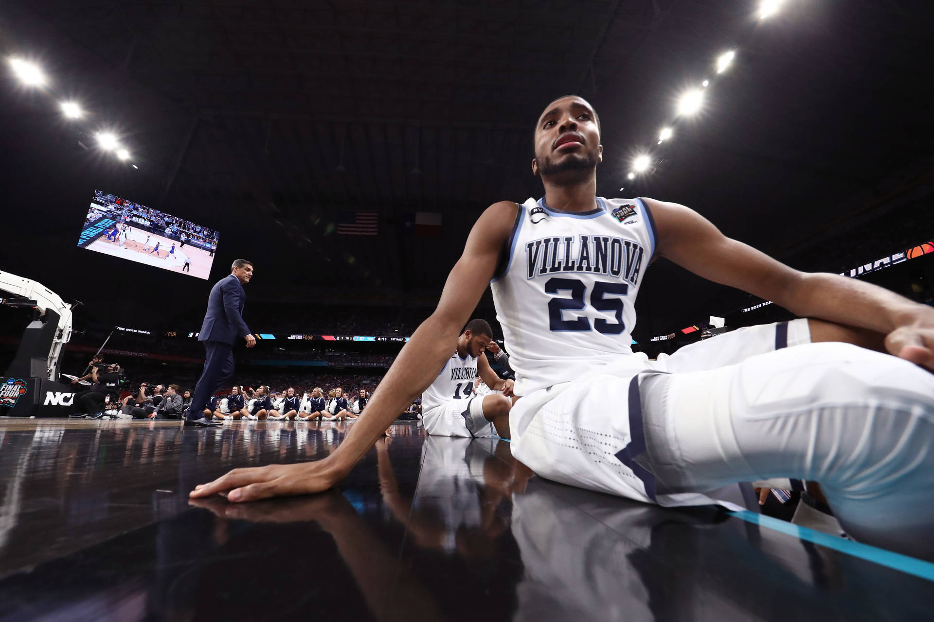 NCAA 維拉諾瓦野貓隊 米卡爾·布里奇斯 壁紙 — 維拉諾瓦大學籃球運動員在比賽結束後，沮喪地坐在明亮的場館燈光下拋光過的球場地板上。