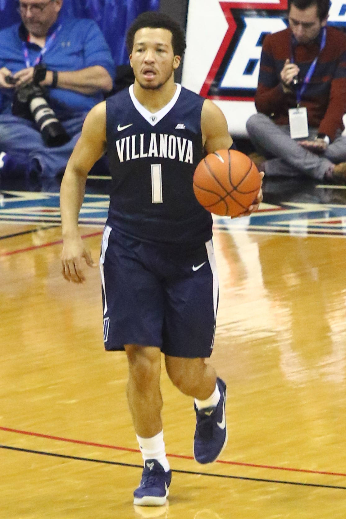 NCAA東區最傑出球員Jalen Brunson 壁紙 — 維拉諾瓦大學籃球運動員身穿海軍藍球衣，在明亮的場館燈光下於室內比賽中運球。