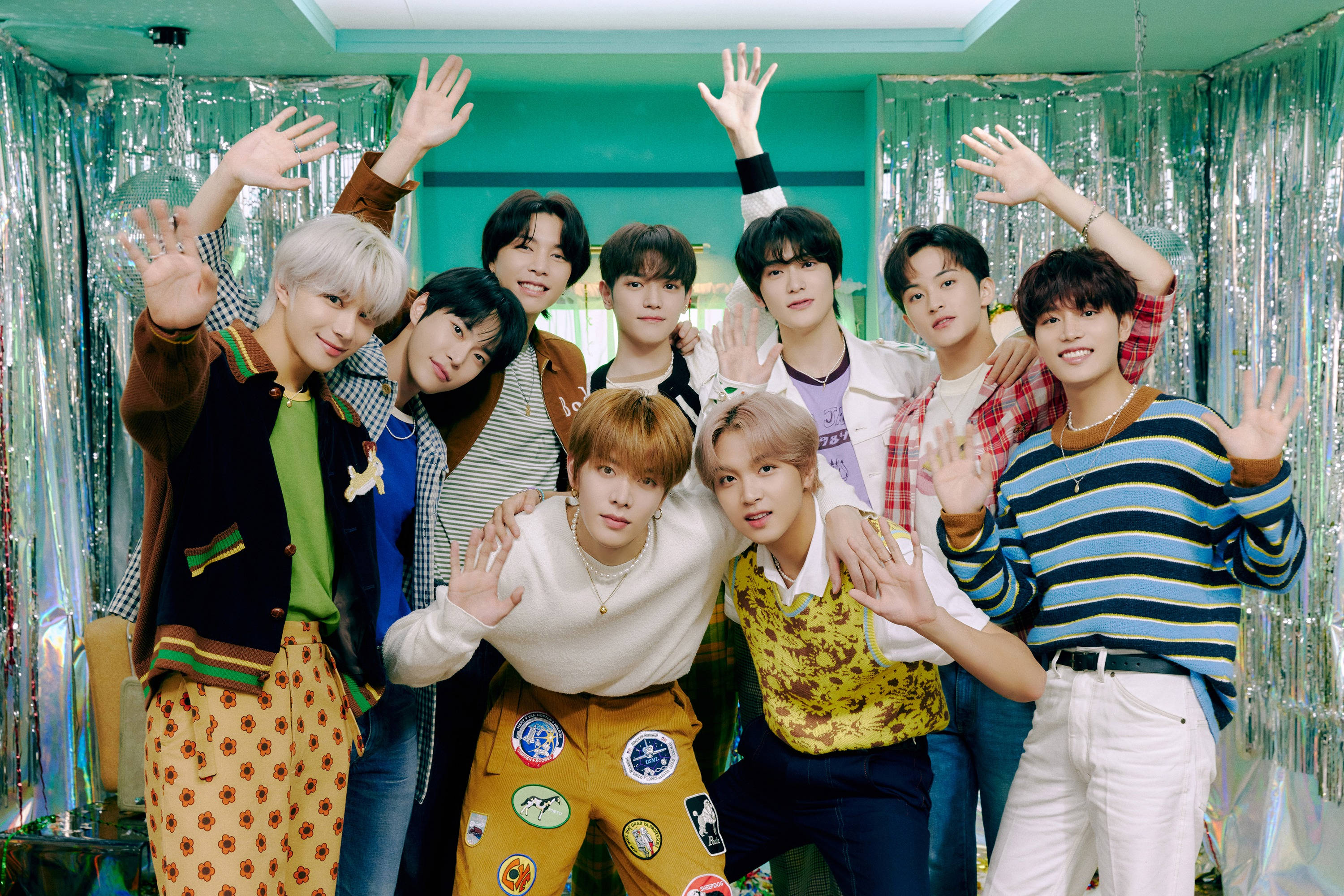 NCT 127《Dreamer》預告影像 壁紙 — 七名身穿色彩繽紛復古服裝的年輕男子，在閃爍的藍綠色背景和銀色亮片窗簾前愉快地揮手。