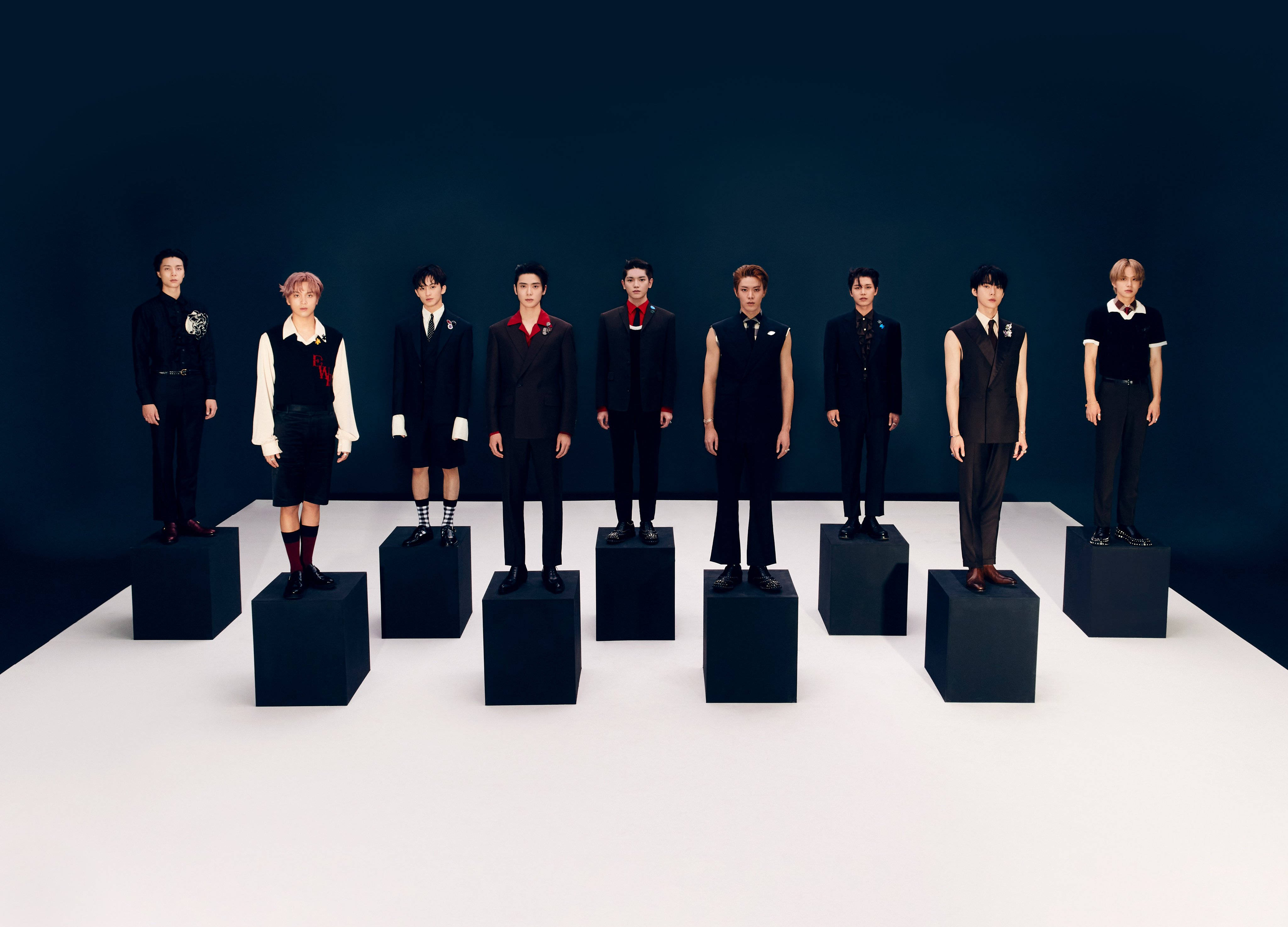 NCT 127《Favorite》重製版經典版概念照 壁紙 — 七位身穿時尚黑色服裝的男士，在深藍色背景襯托下，從容地站在黑色底座上。