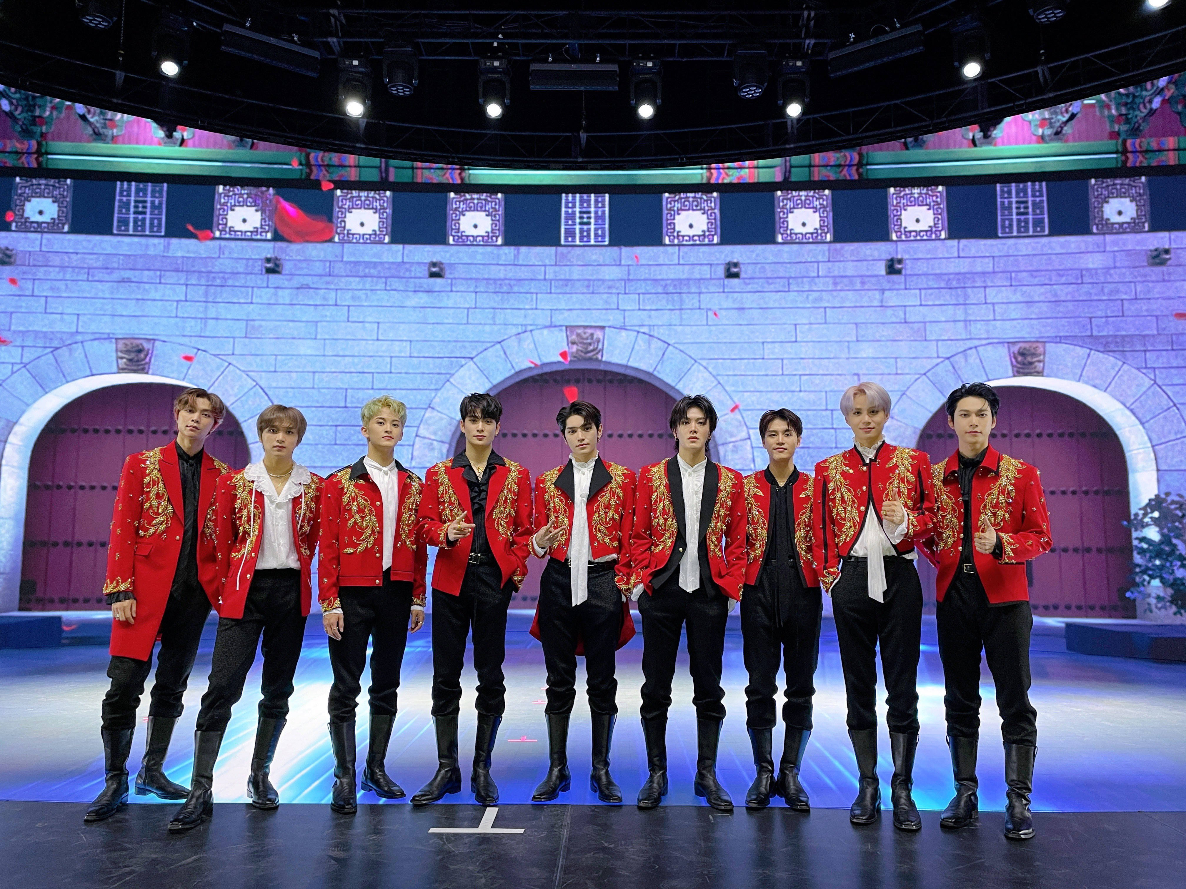 NCT 127《Favorite》2021 MAMA 舞台照 壁紙 — 七名身穿華麗紅色外套的男子在城堡主題背景和發光藍色地板的舞台上自信地擺姿勢。