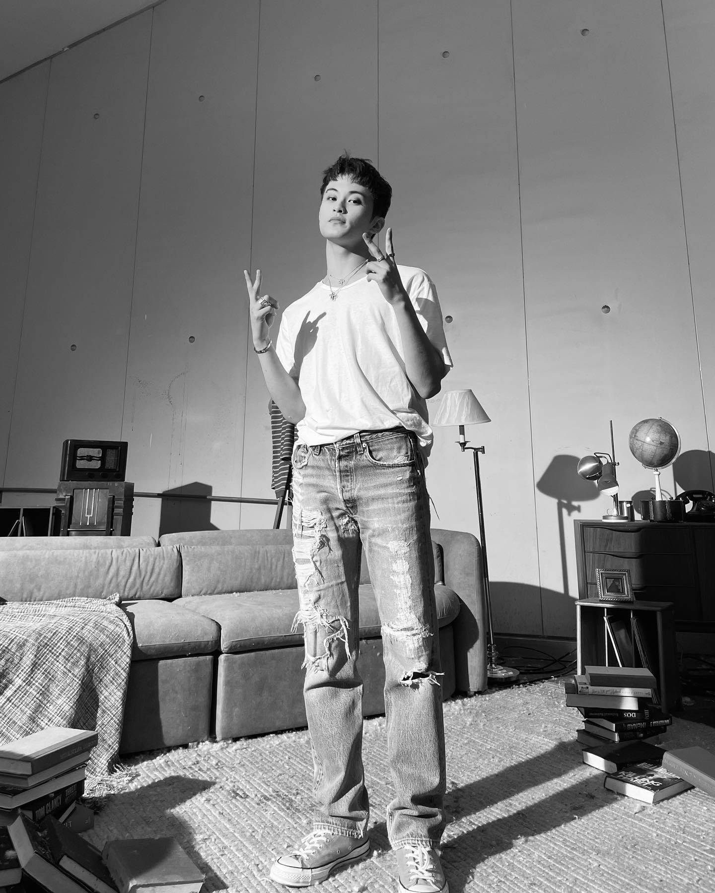 NCT 127 Mark《Child》單曲照 壁紙 — 一位穿著破洞牛仔褲和白色T恤的年輕男子，在陽光充足的簡約房間裡自信地站著，比出和平手勢。