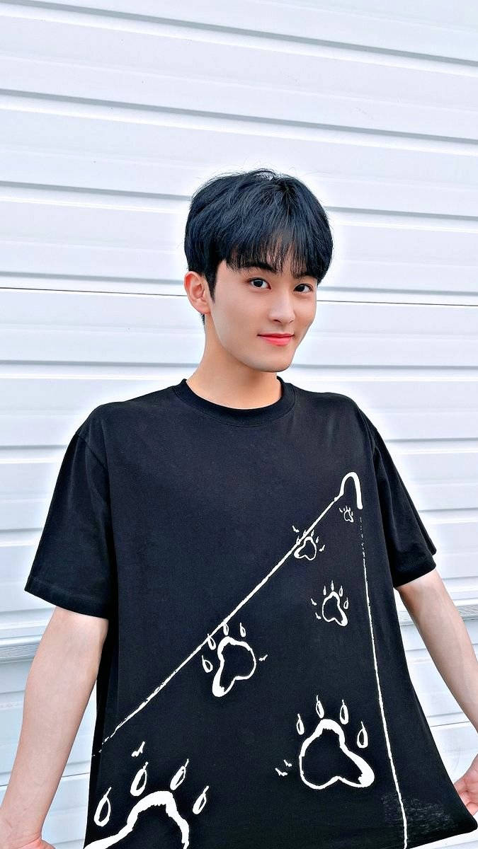 NCT 127 Mark 身穿經典腳印襯衫 壁紙 — 一位黑髮年輕男子微笑著，身穿印有白色爪印和雨滴圖案的黑色T恤，背景是白色波紋牆。