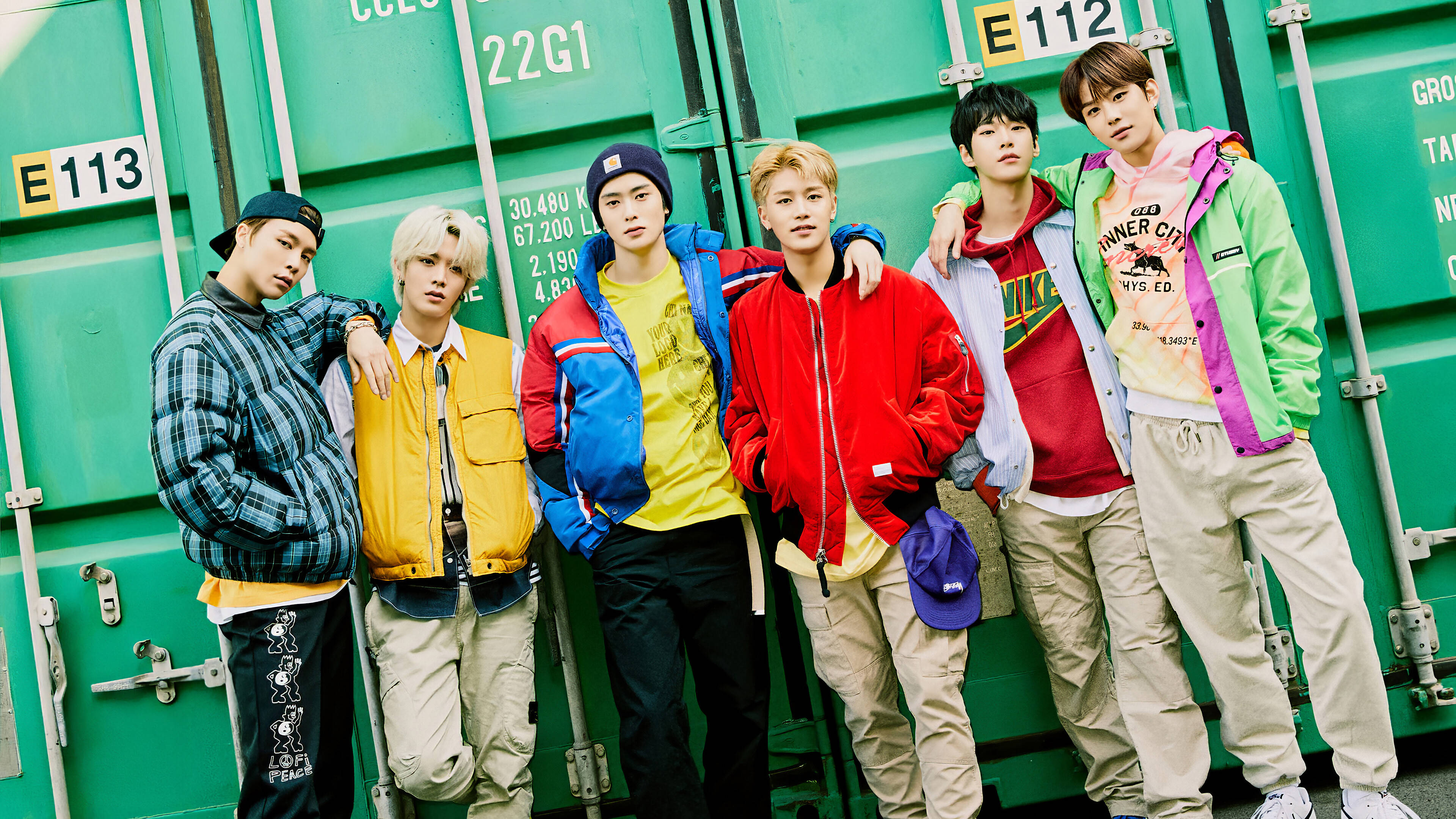 NCT 127 Neo Zone 時代 壁紙 — 五位時尚年輕男子身穿色彩繽紛的街頭服飾，在充滿活力的綠色貨櫃背景前自信地擺姿勢。