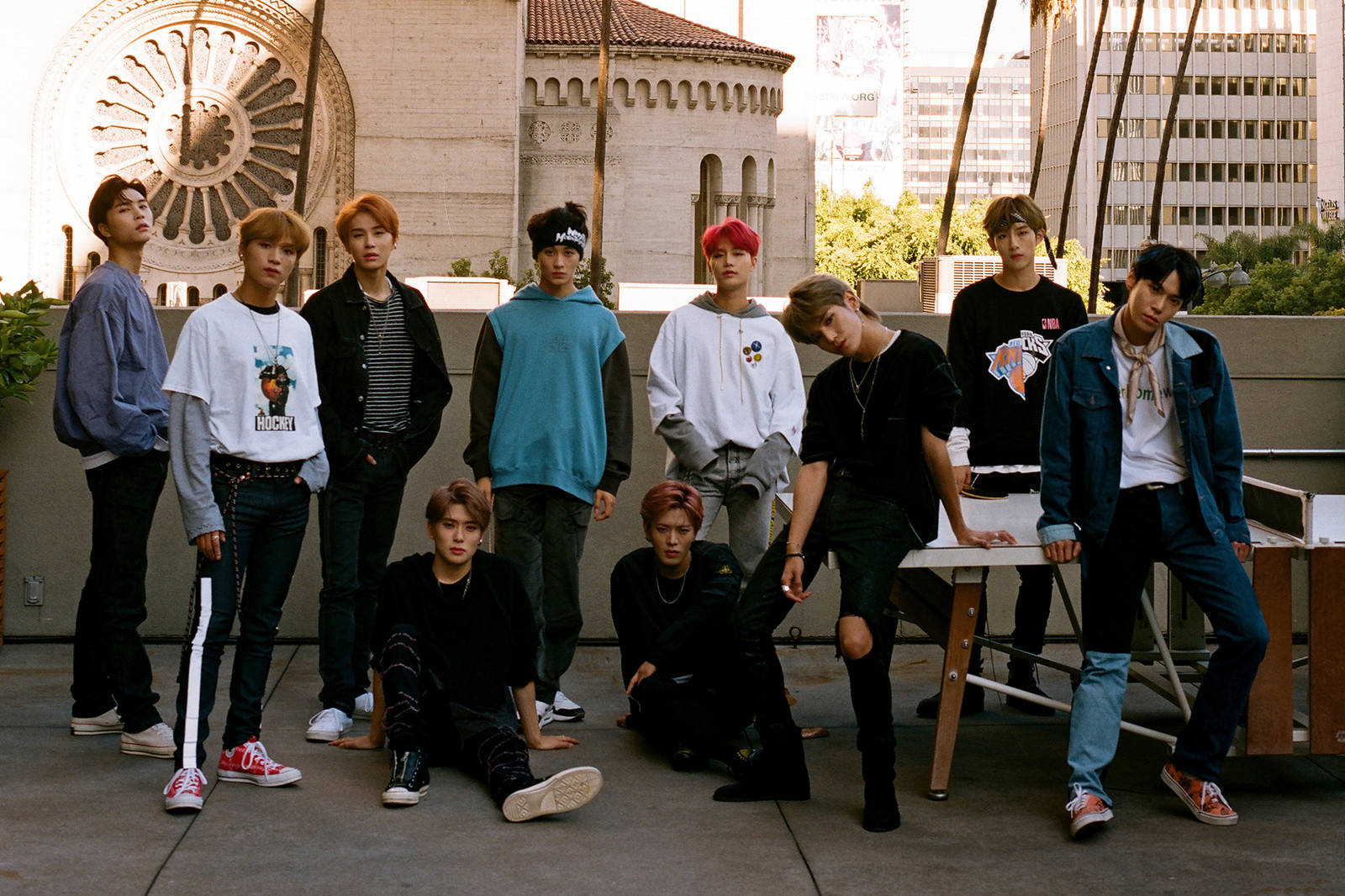 NCT 127 Regular-Irregular時代 壁紙 — 七位身穿休閒街頭服的年輕男性在屋頂上自信地擺姿勢，背景是歷史建築和棕櫚樹。