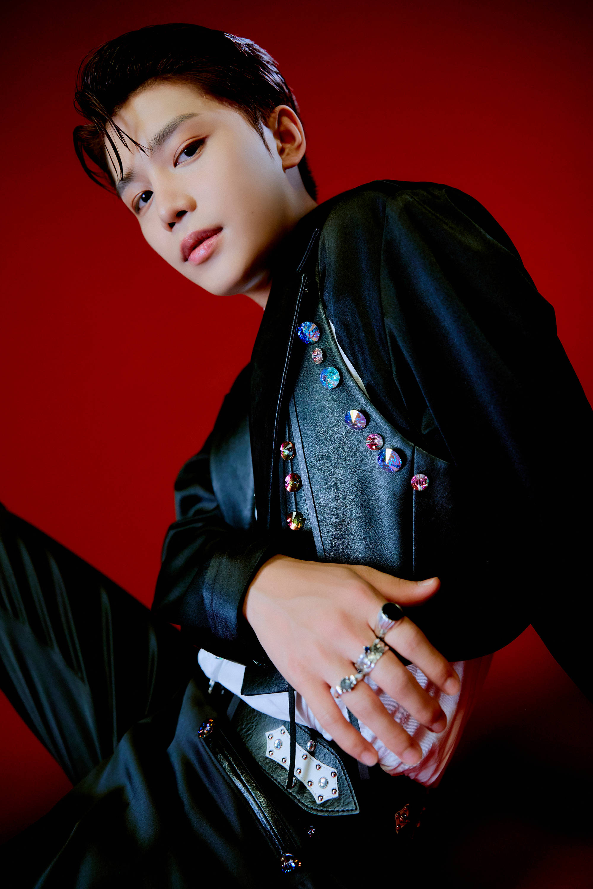 NCT 127 Taeil《Sticker》預告照 壁紙 — 一名年輕男子身穿飾有彩色寶石的黑色皮褸，在鮮紅色背景前自信地擺姿勢。