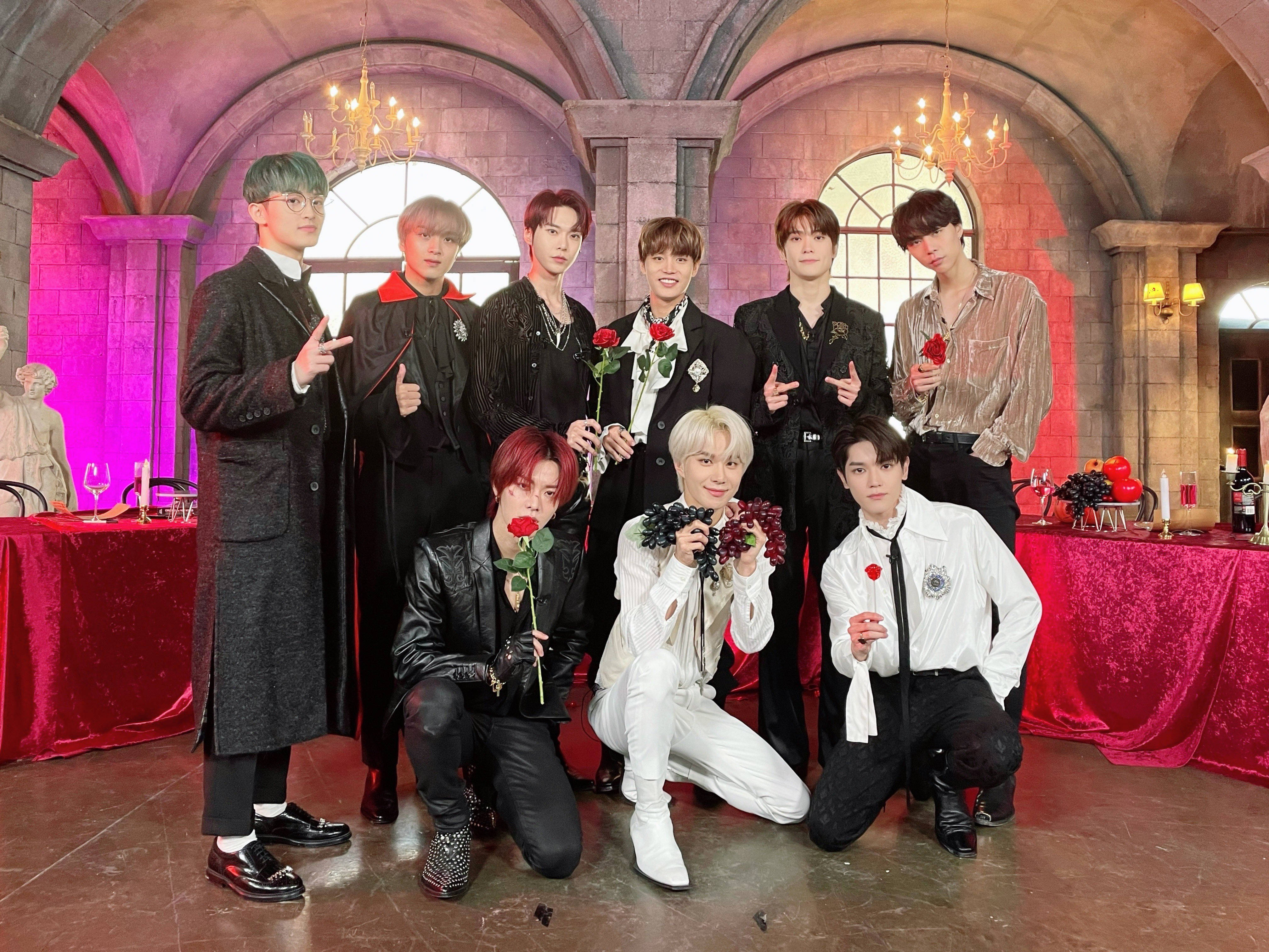 NCT 127《Vampire House》造型照 壁紙 — 七位時尚男士穿著正式服裝，在一個宏偉的哥德式大廳中，與紅玫瑰和葡萄一起擺姿勢，大廳內有吊燈和紅色天鵝絨桌子。