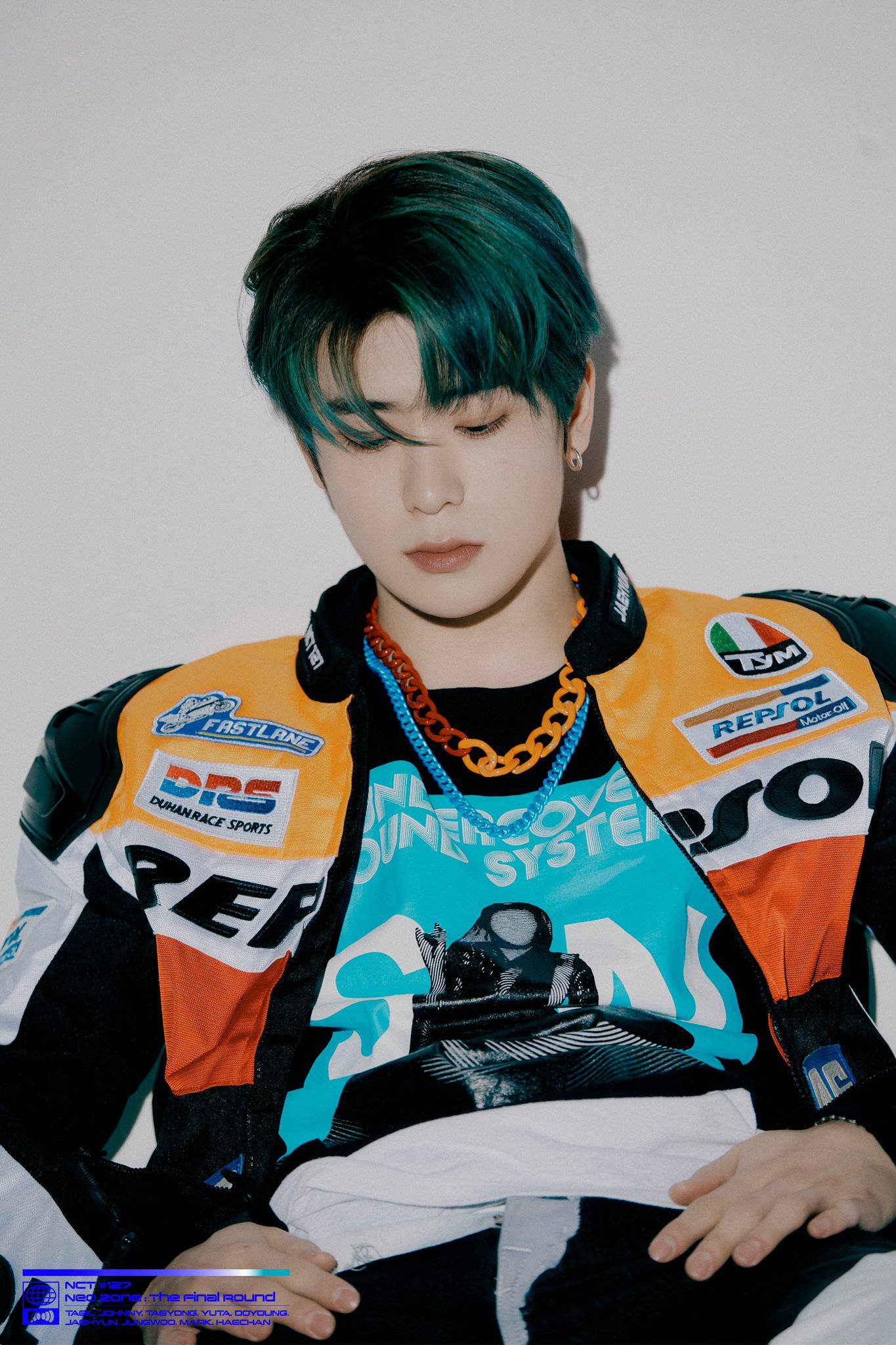 NCT 127 成員 JaeHyun《Neo Zone》攝影棚照 壁紙 — 一位年輕男子留著藍綠色頭髮，穿著色彩繽紛的賽車夾克，站在純白牆壁前。
