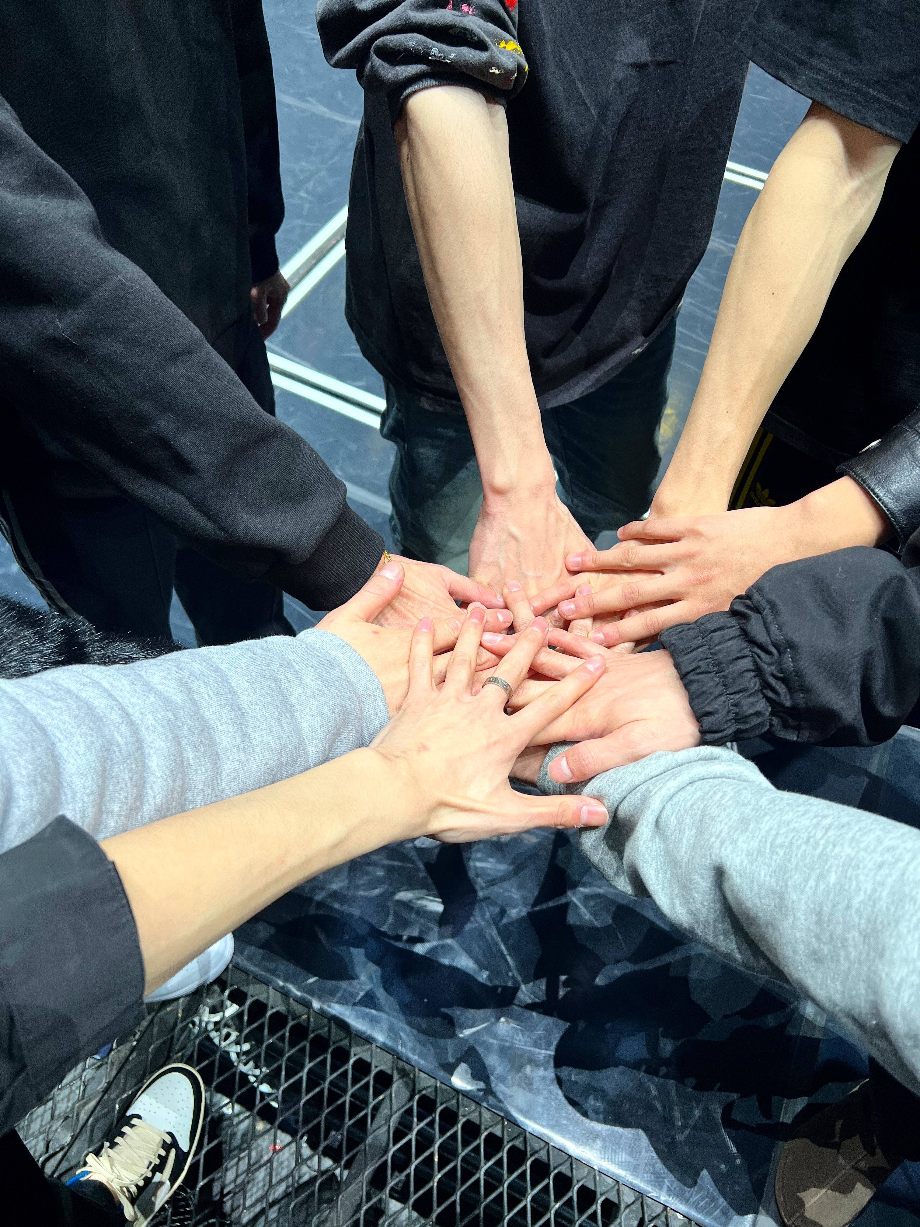 NCT 127 搏鬥 壁紙 — 五個人在明亮的日光下將手疊成一個圓圈放在反光表面上。