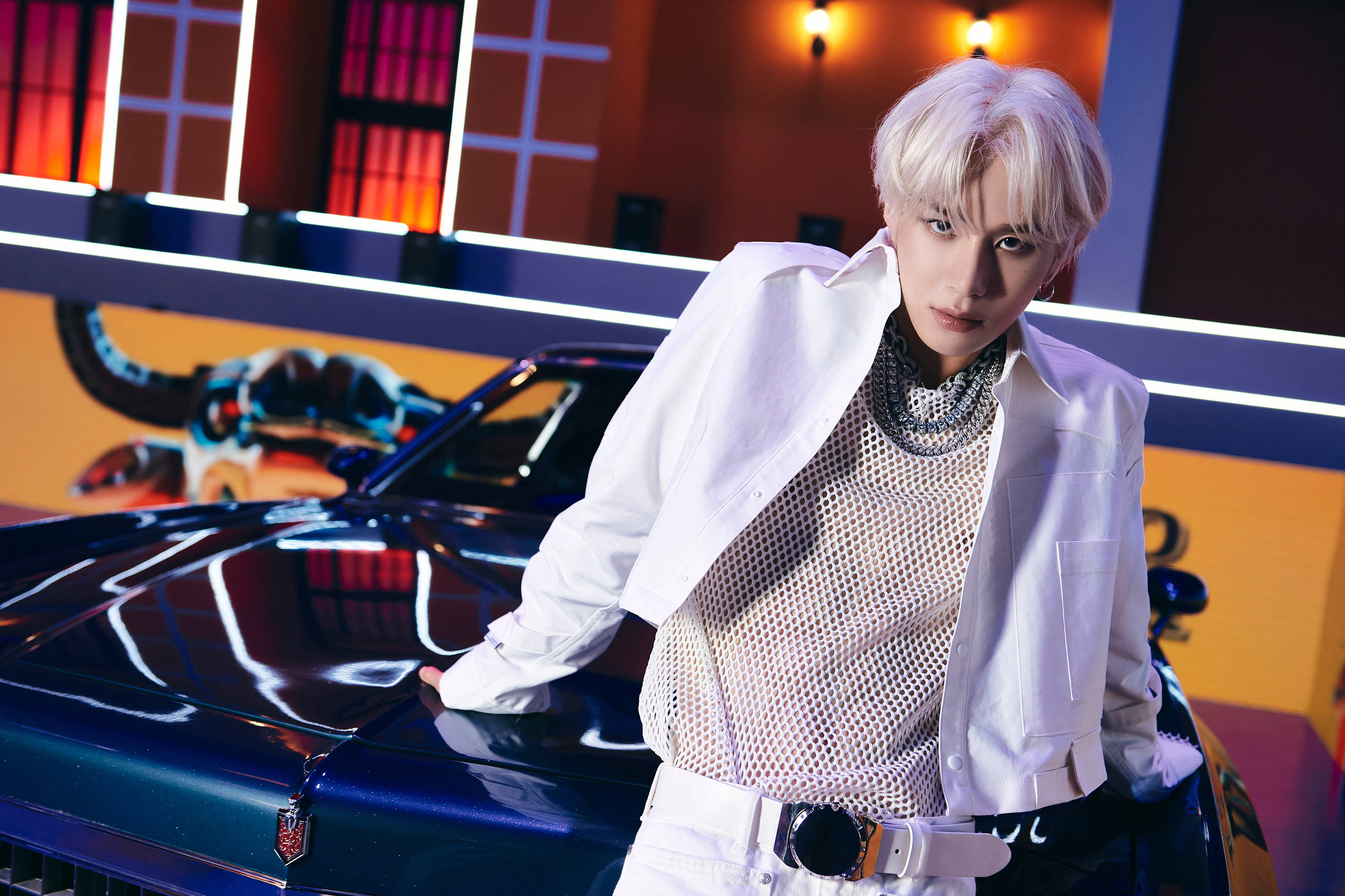 NCT 127 洪知秀貼紙預告 壁紙 — 一個擁有鉑金色頭髮的人自信地靠在一輛閃亮的藍色跑車上，身處一個帶有橙色和紫色燈光的霓虹燈工作室。