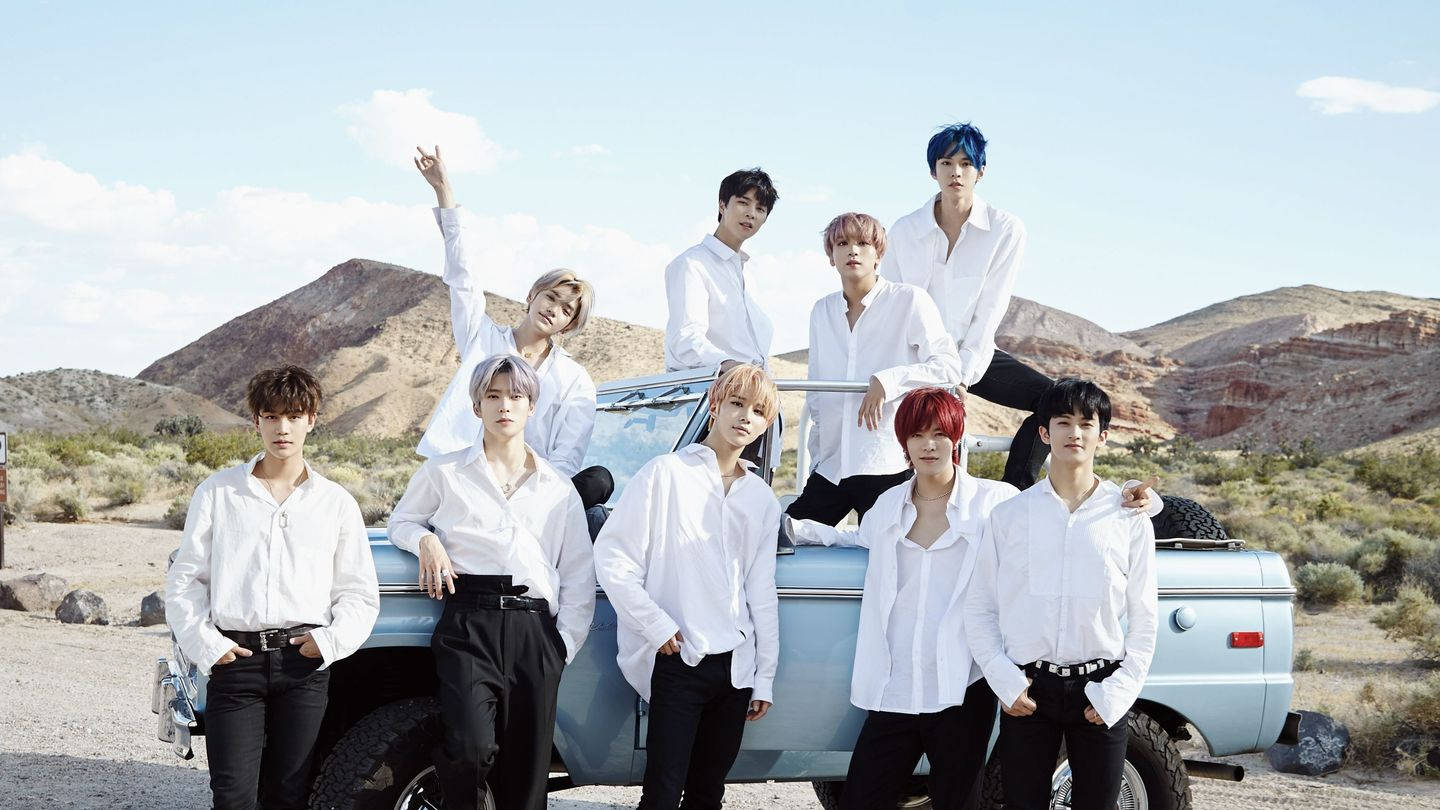 NCT 127《通往天堂的高速公路》 壁紙 — 七個身穿白恤衫嘅年輕男子喺陽光普照嘅沙漠峽谷中，自信地企喺一架淺藍色復古貨車周圍擺甫士。
